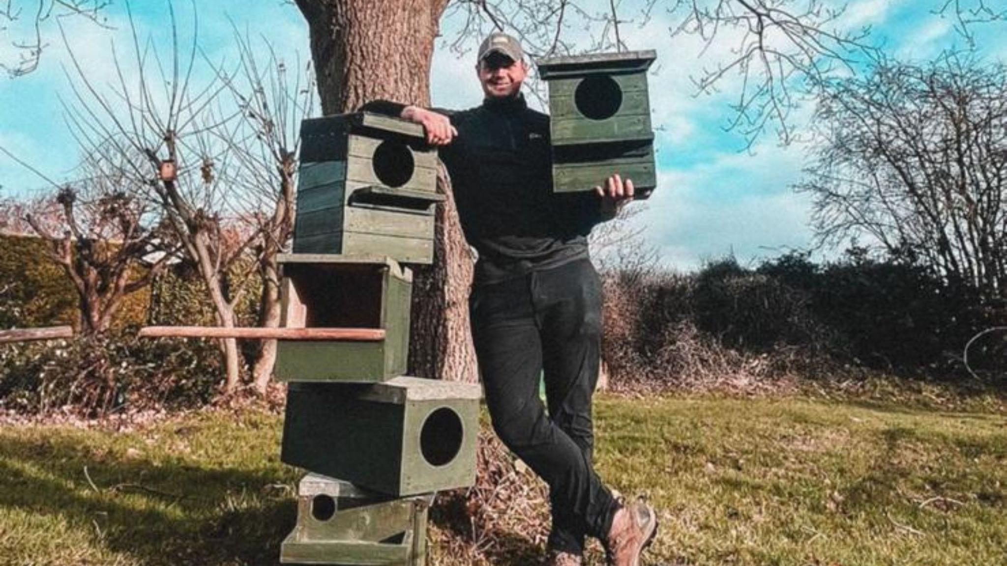 Will is leaning on a stack of wooden bird boxes.