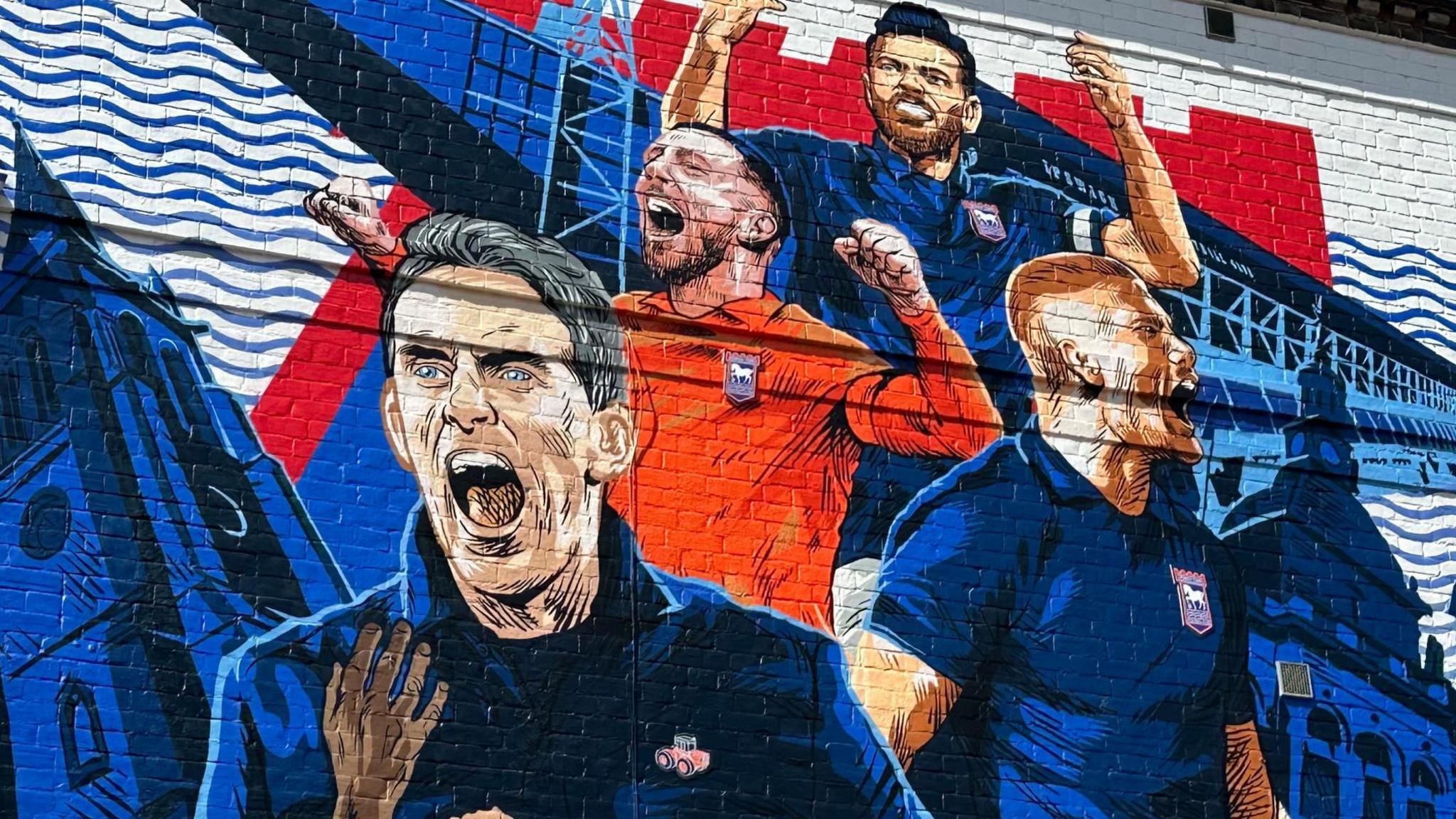 A close-up of a mural painted on the side of a building. The artwork includes Kieran McKenna, three other players and is mostly blue.