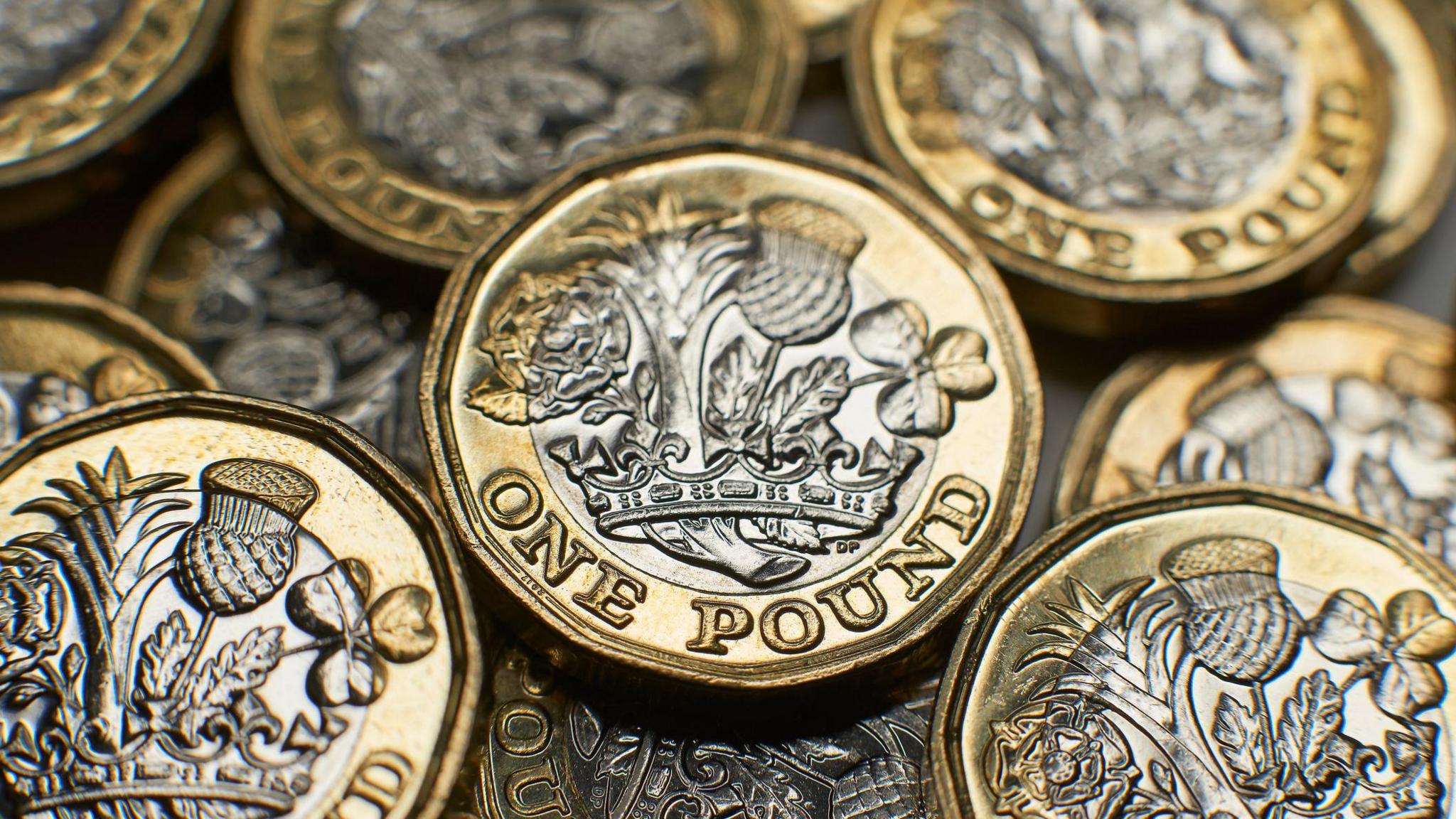 A pile of one pound coins. They each feature a gold border with silver in the middle. An emblem is imprinted on them.