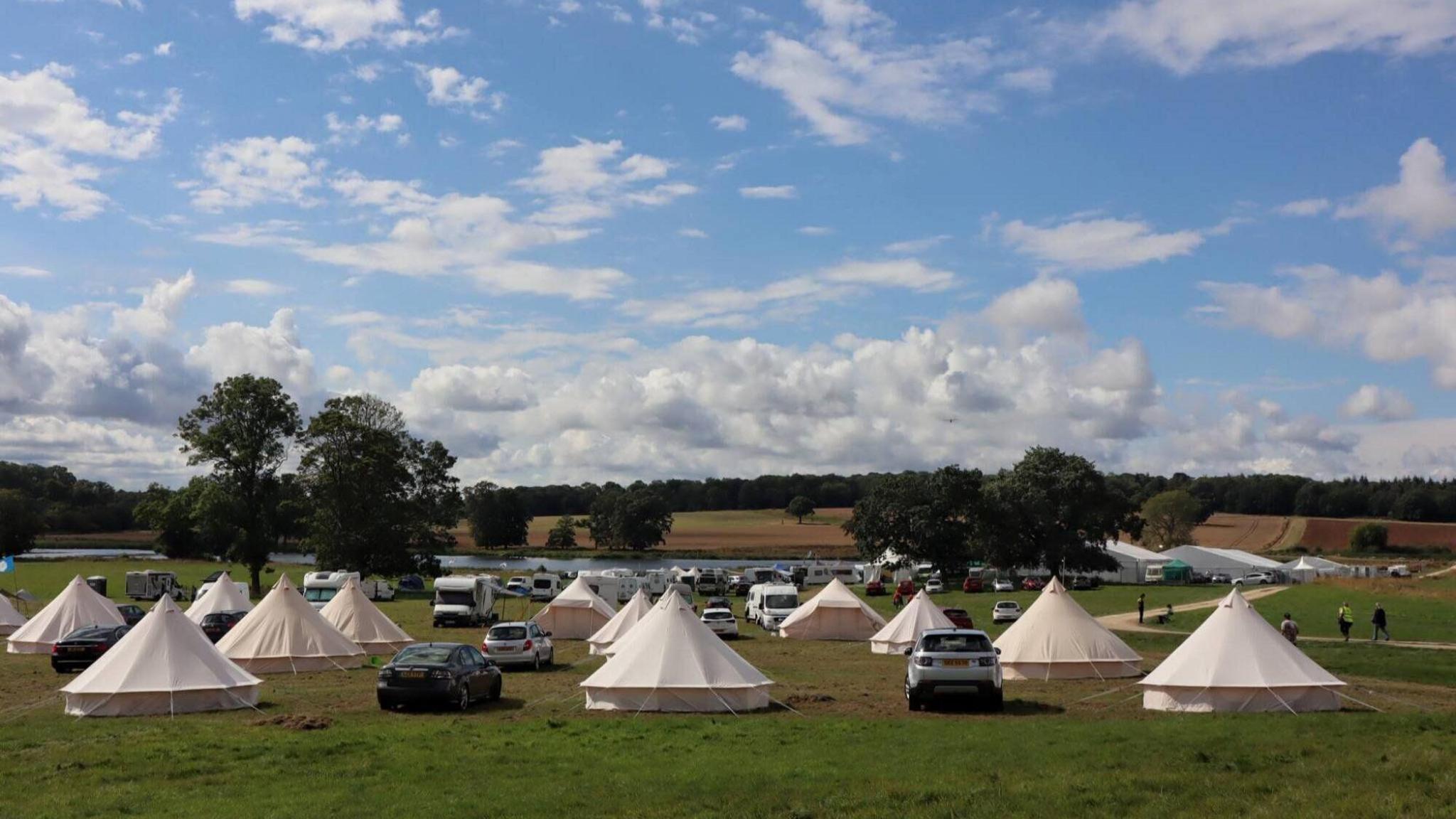 A field under a blue sky, with about a dozen white glamping pods.