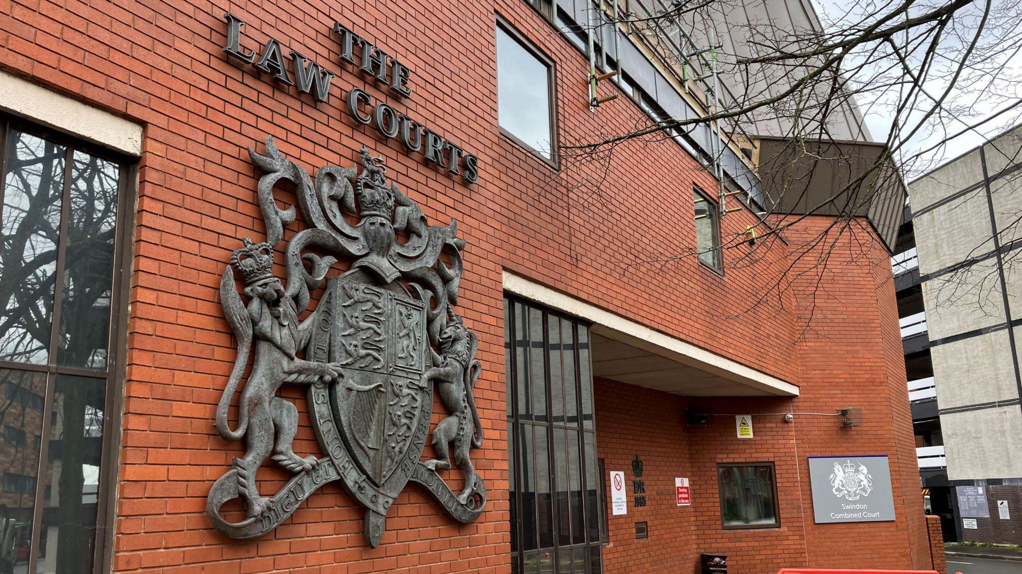 The exterior frontage of Swindon Crown Court, with red bricks and a large legal insignia 