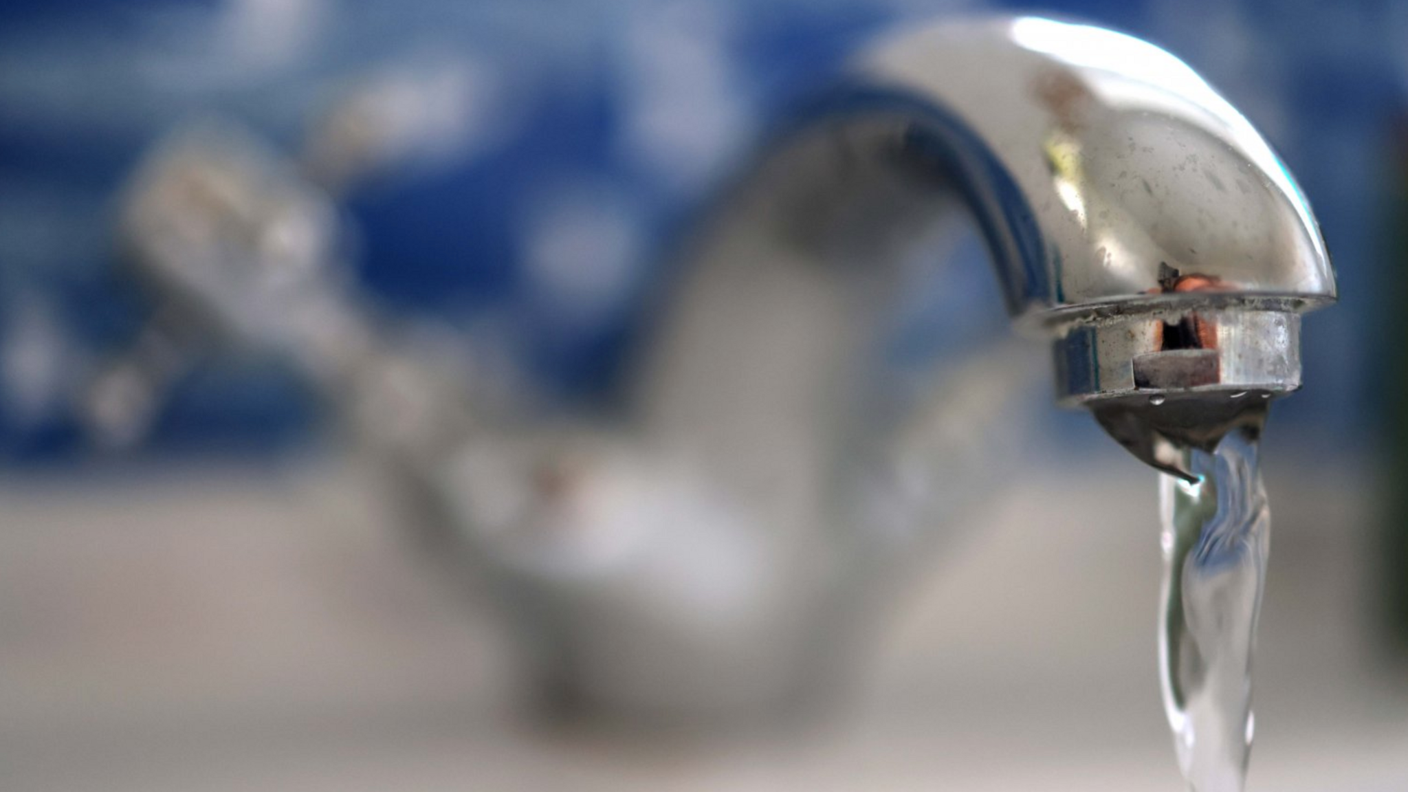 A water tap with water running out of it with a blurred background.