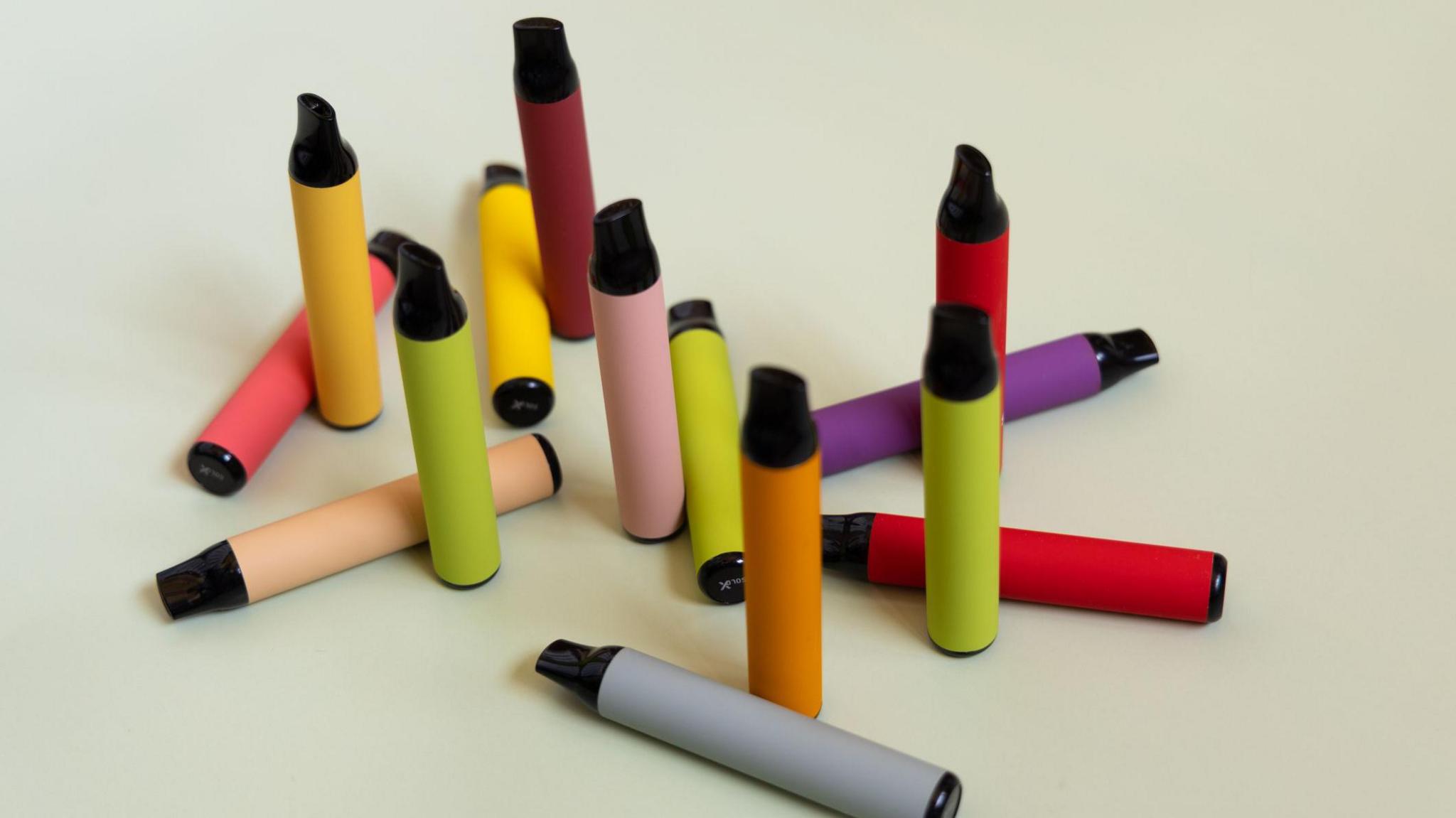 An assortment of multicoloured vapes arranged on a white surface.