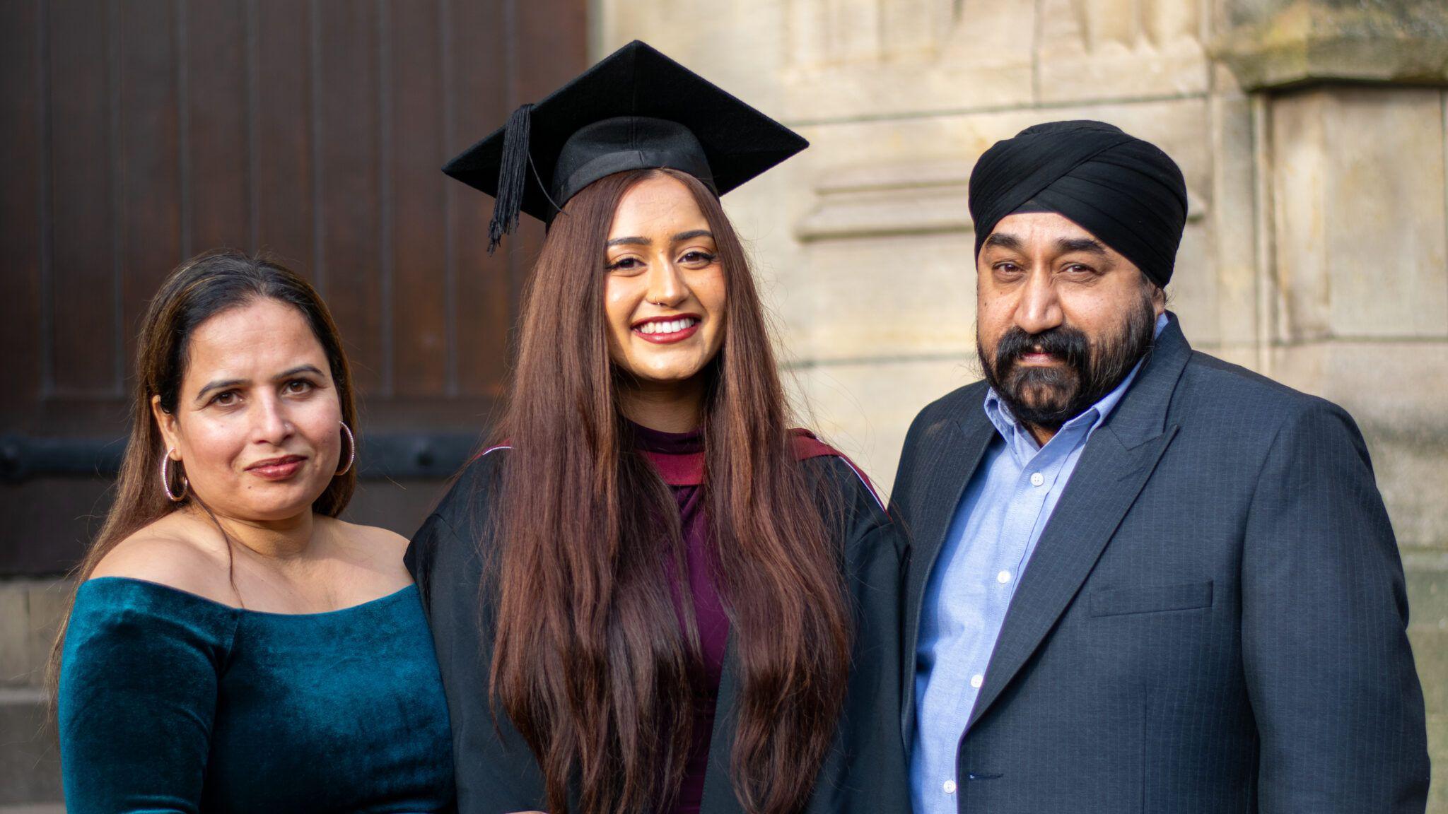 A woman wearing a mortar board smiles to the camera, with family either side of her