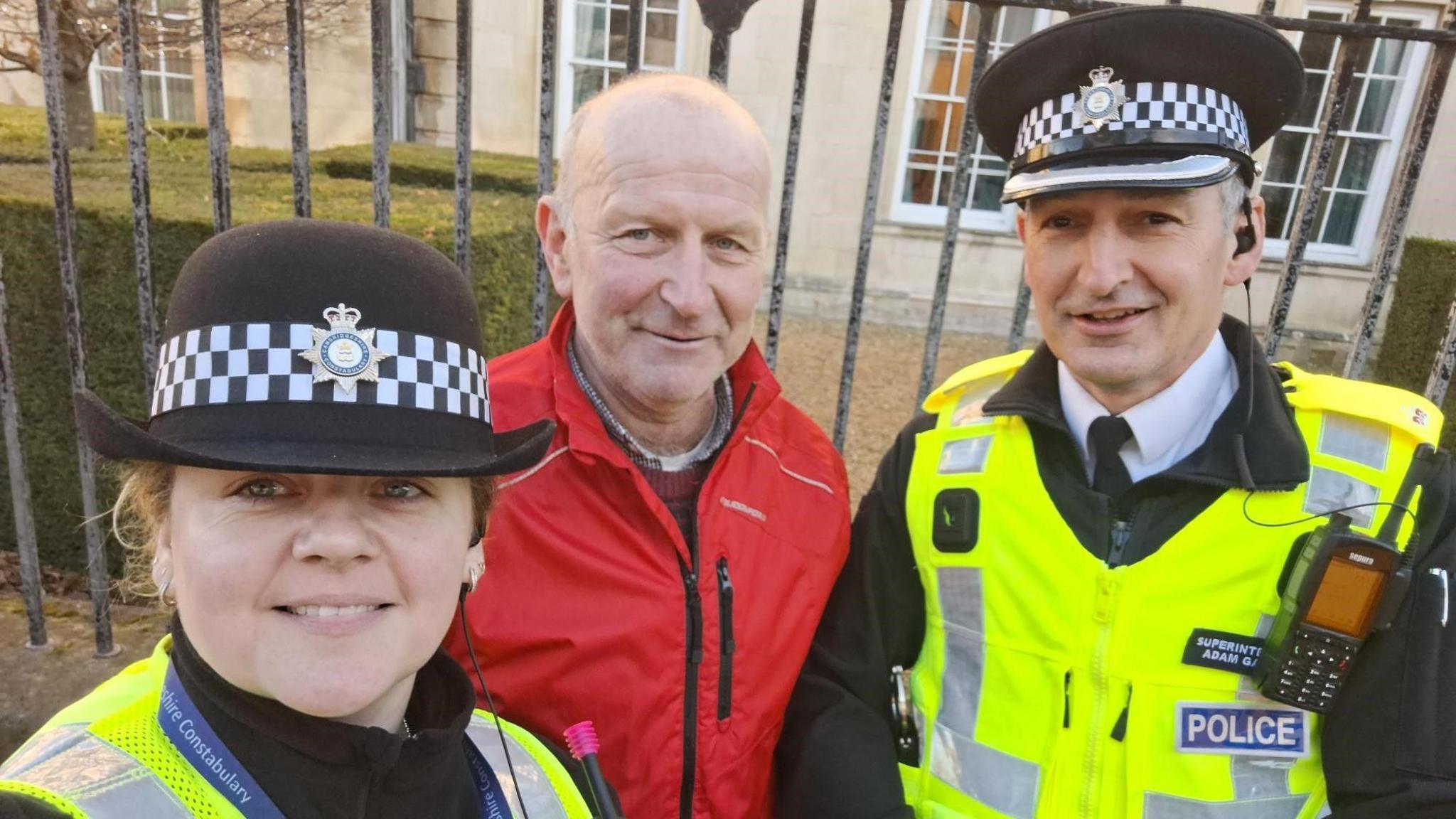 A woman police officer in a high-visibility green jacket and a man wearing a red coat and a policeman in his green and black uniform - smiling at a selfie 