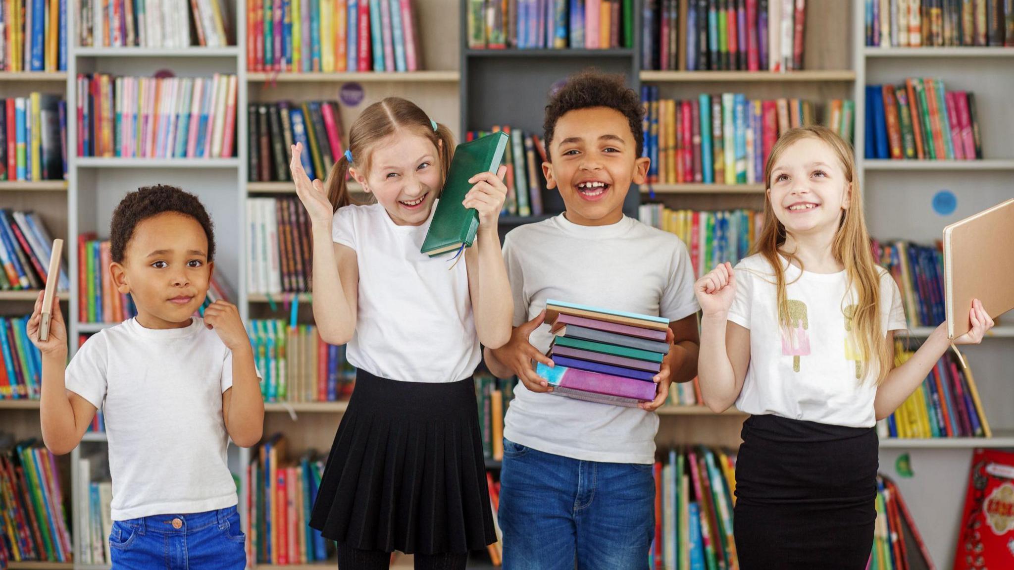 Four children stand in a line in front of a colourful book shelf smiling