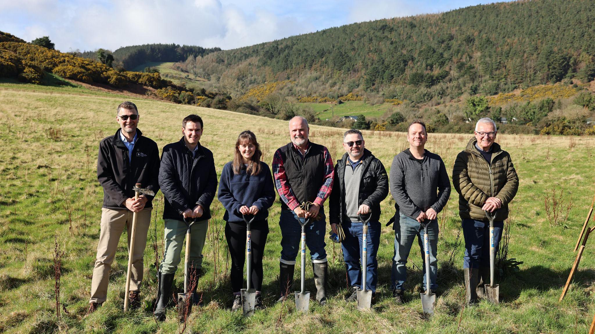 Seven people standing in a field with spades