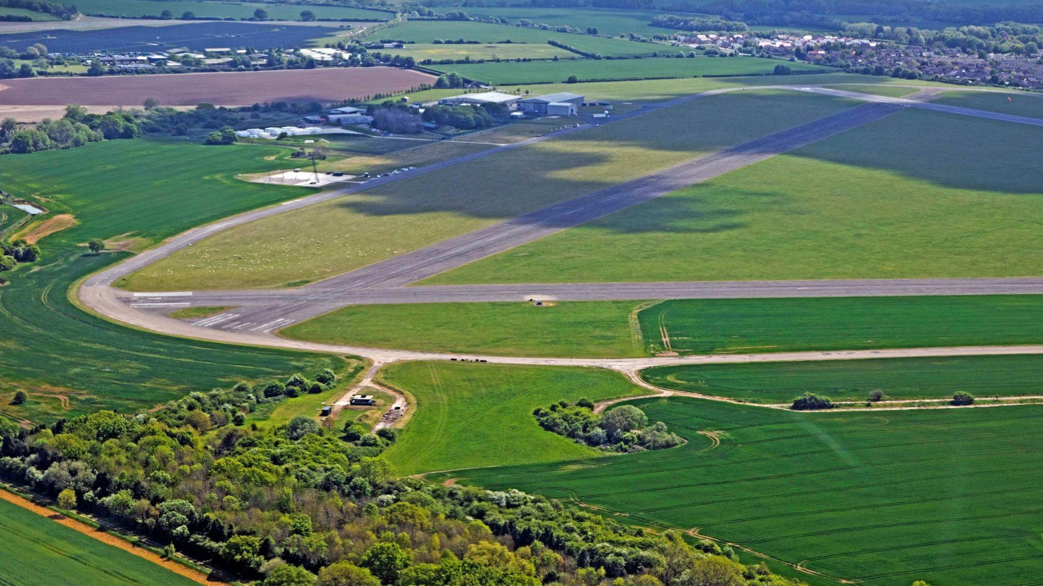 Another bird's eye view of Chalgrove Airfield, including two runways, surrounded by countryside and, in the top right corner, the village of Chalgrove