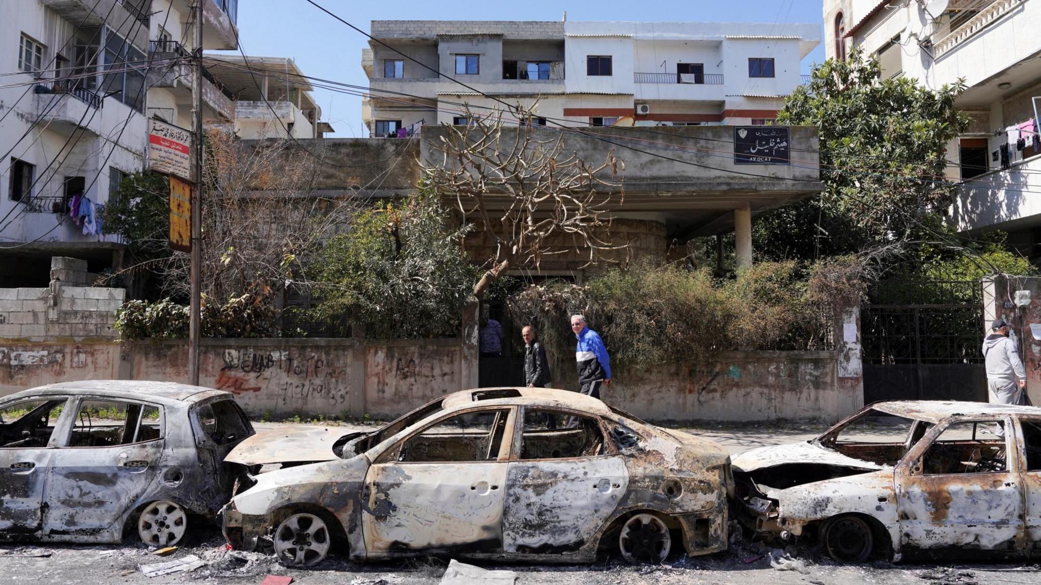 File photo showing people walking past burned-out cars in Jableh following the mass killing of Alawites in Syria's north-west coastal region (12 March 2025)