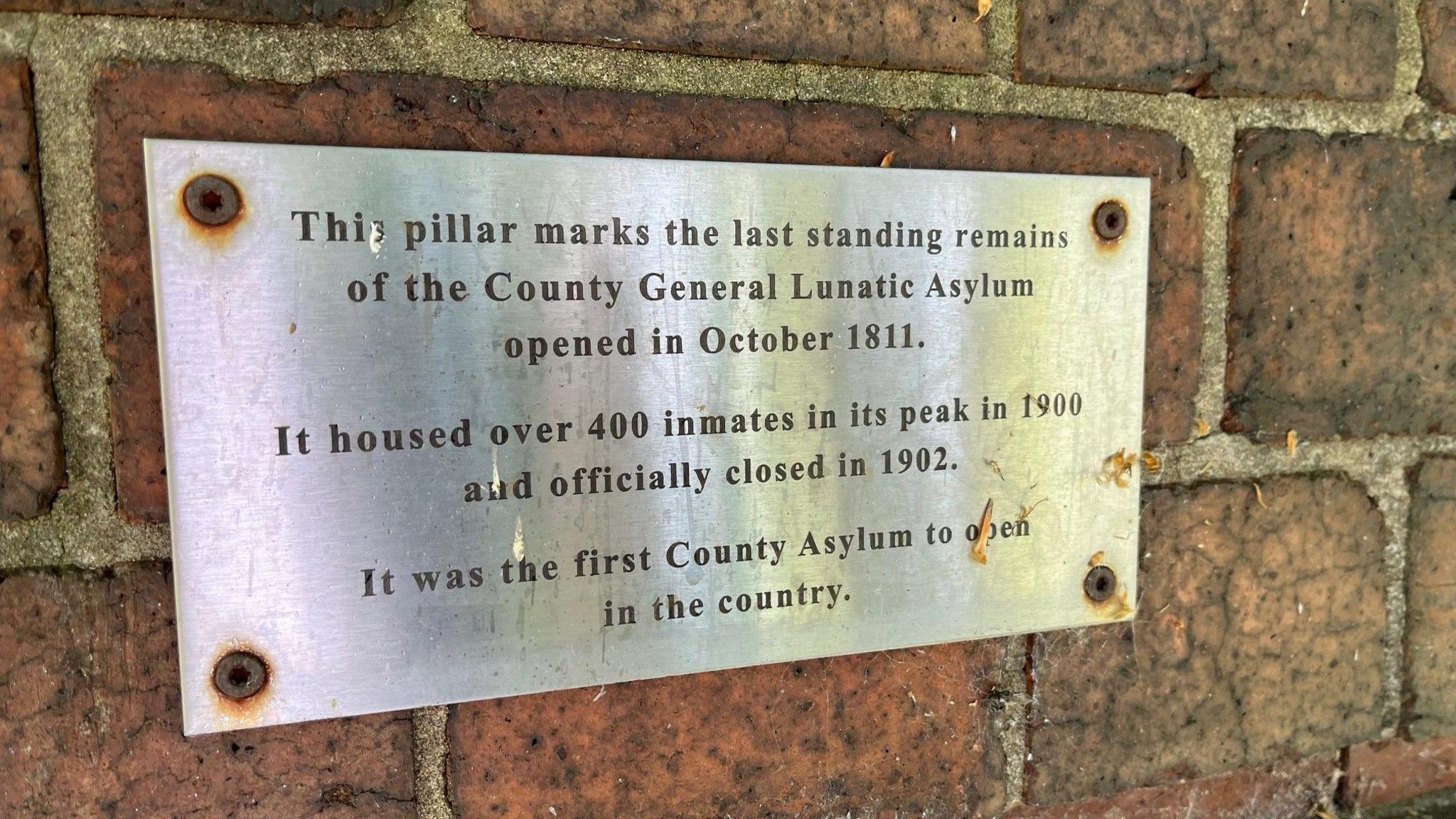 Metal plaque explaining that the brick pillar it is mounted on is the last fragment of the original Nottingham Asylum