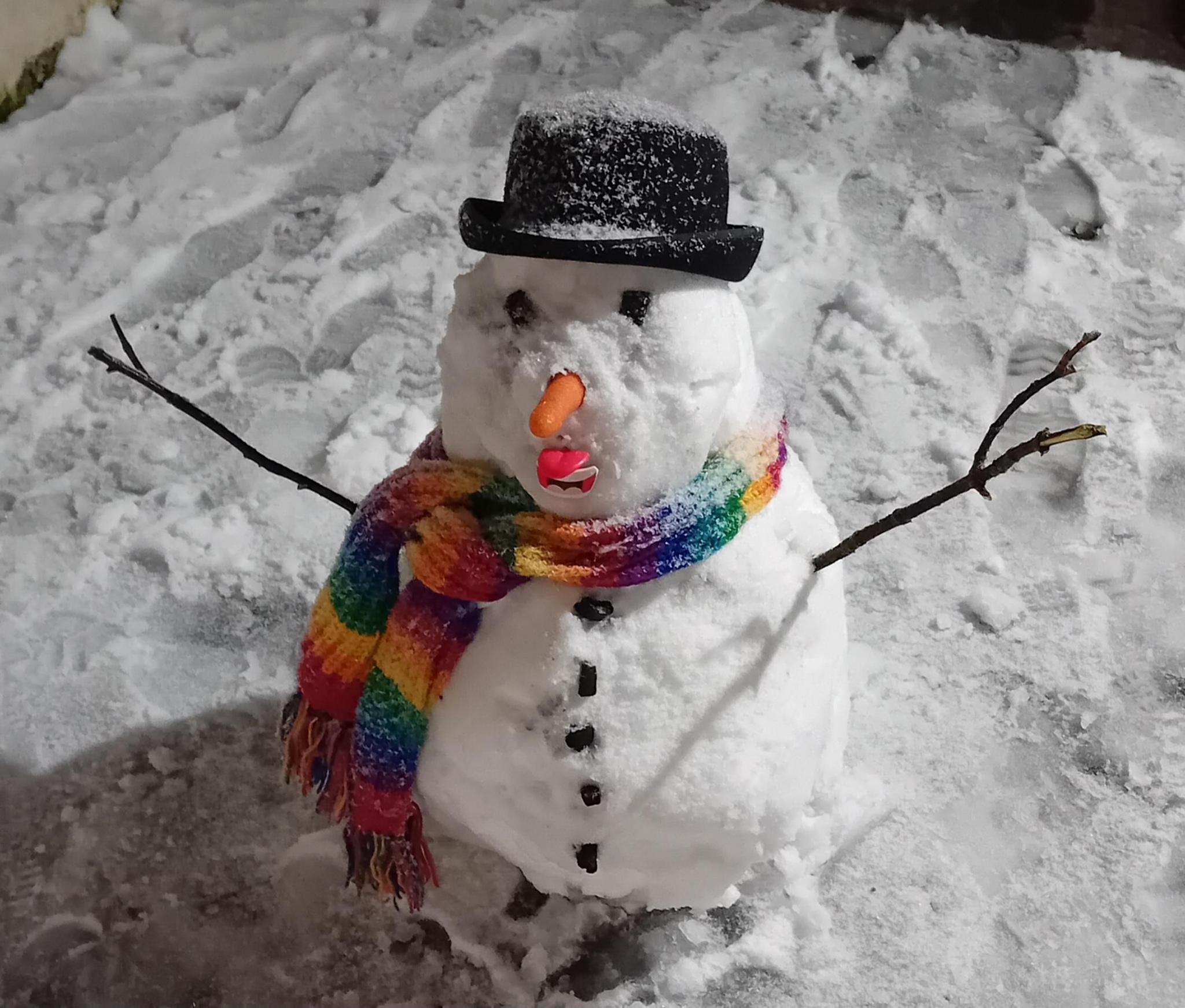 A snowman wearing a black bowler hat and rainbow scarf