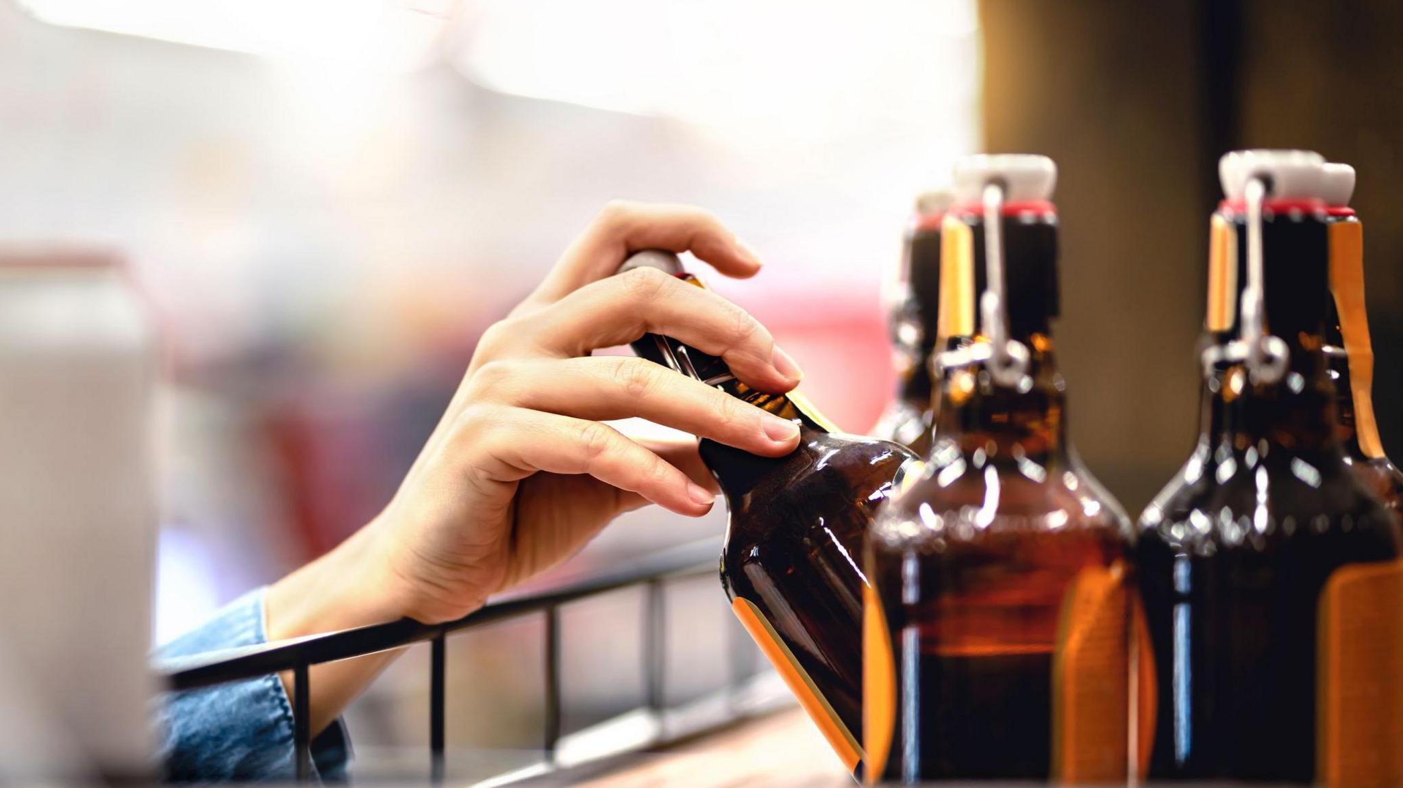 A hand reaching up on a shelf for a bottle of craft cider