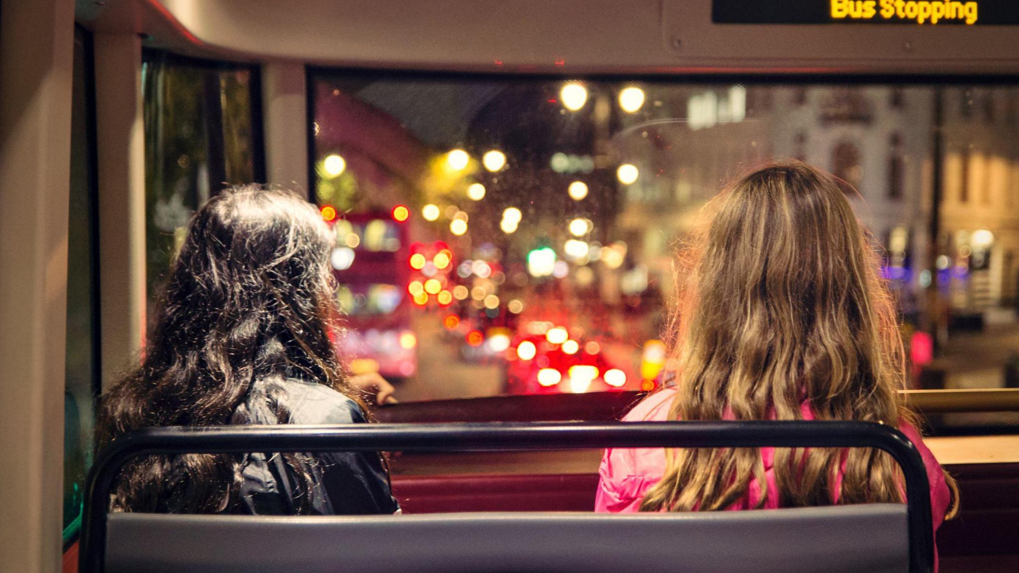 the back of two young women's head. they are sitting on a bus at night looking onto traffic