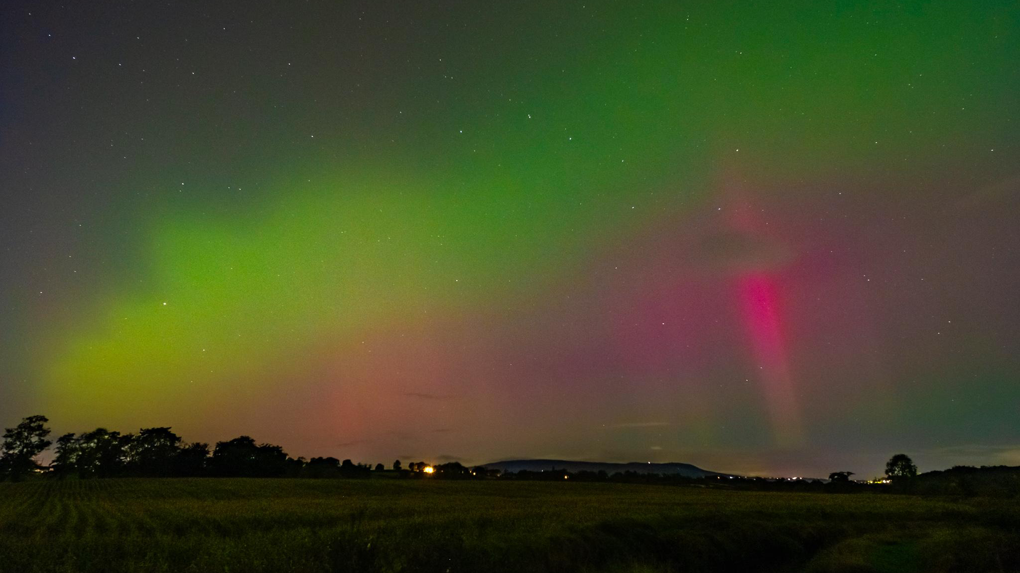 The Northern Lights visible in the sky, which is blue, green and pink. 