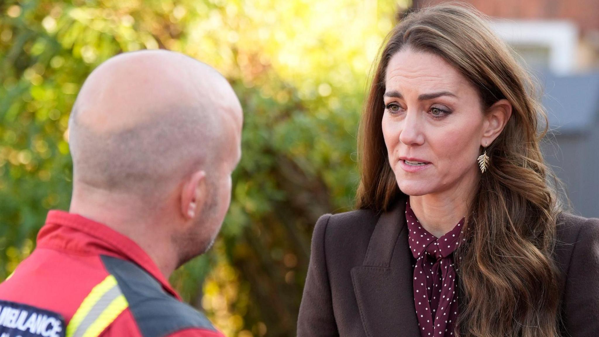 The Princess of Wales with her long brown hair down wearing a brown polka dot blouse and brown coat speaks with a paramedic from the Air Ambulance during a visit to Southport Community Centre to meet rescue workers and the families of those caught up in the Southport knife attack