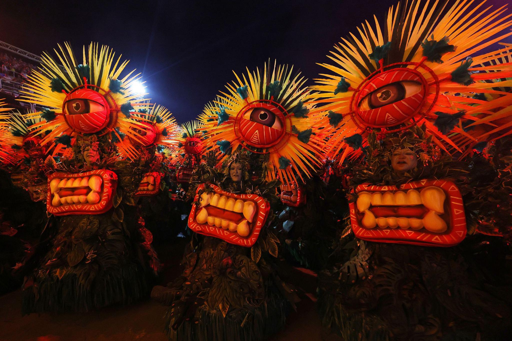 Three members of Grande Rio perform wearing costumes involving giant single eyes and teeth.