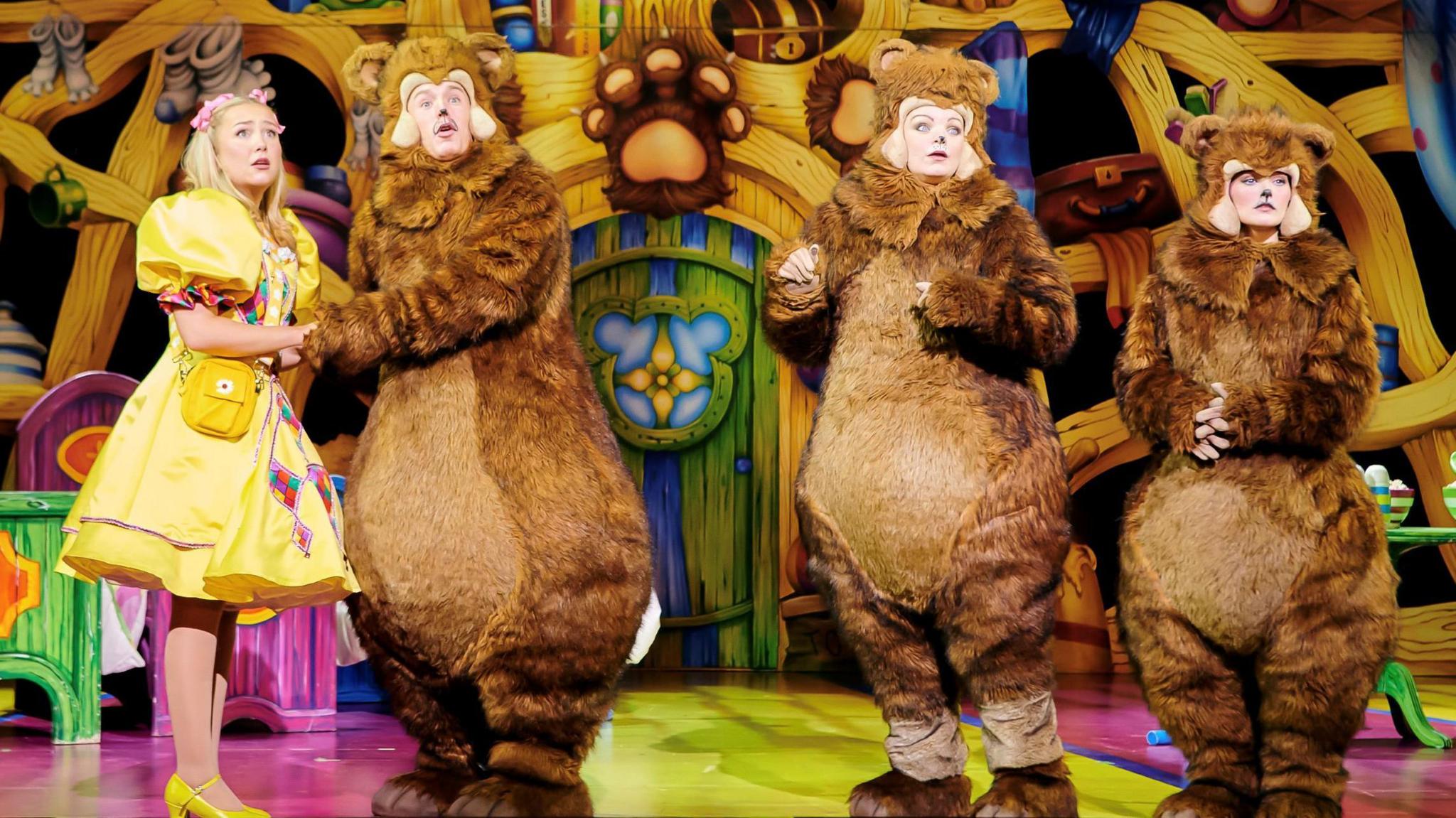 Actors playing roles in Goldilocks at the Three Bears at the Bristol Hippodrome stand on stage looking concerned. One is dressed as Goldilocks and the other three are in brown bear costumes