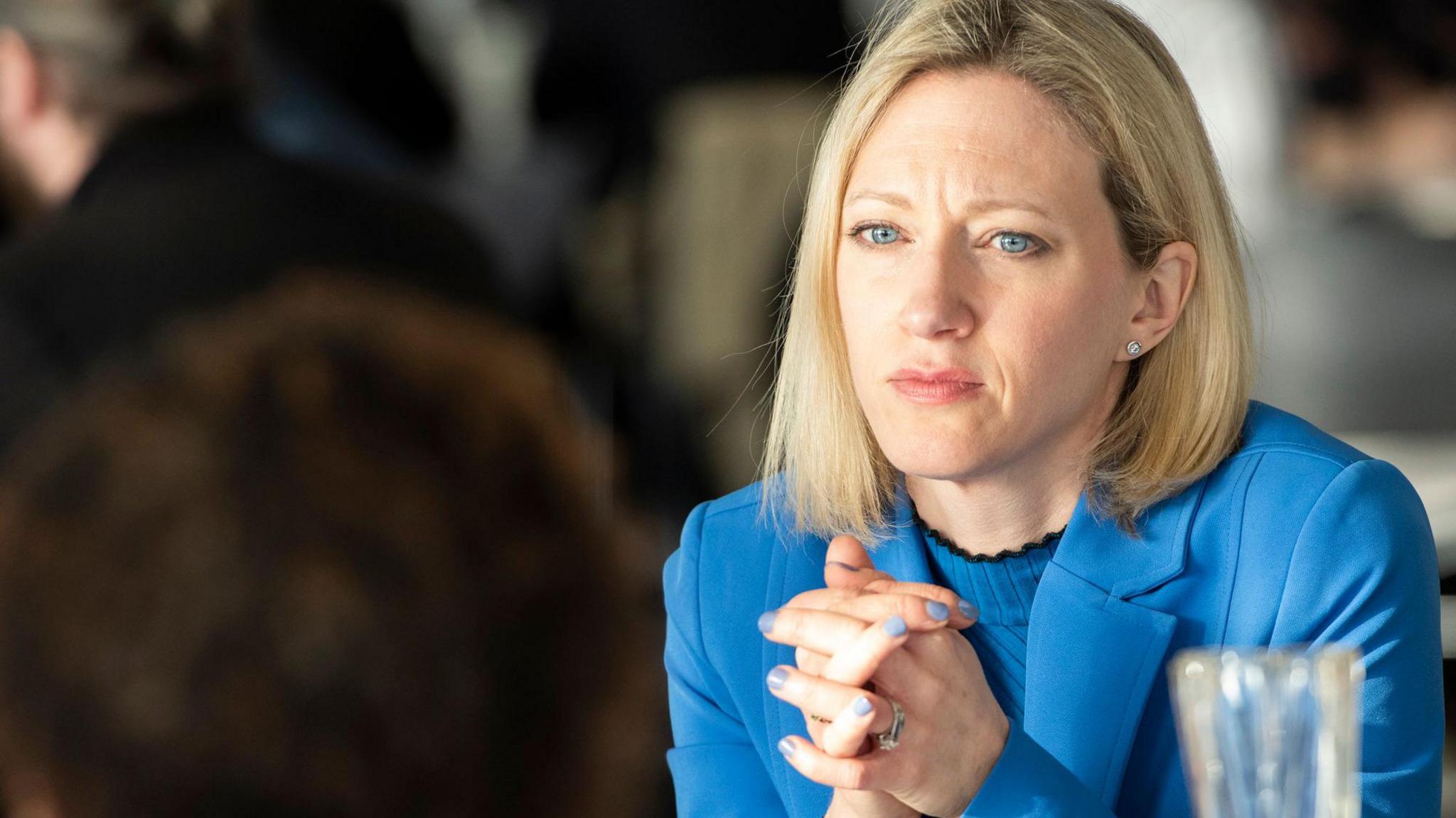 Official image of Claire Waxman. She wears a bright blue jacket and top, and has her hands interlaced in front of her. Her fingernails are painted blue. She looks smartly groomed with shoulder-length blonde hair and blue eyes, and has an earnest expression on her face as if she is listening to a concern.