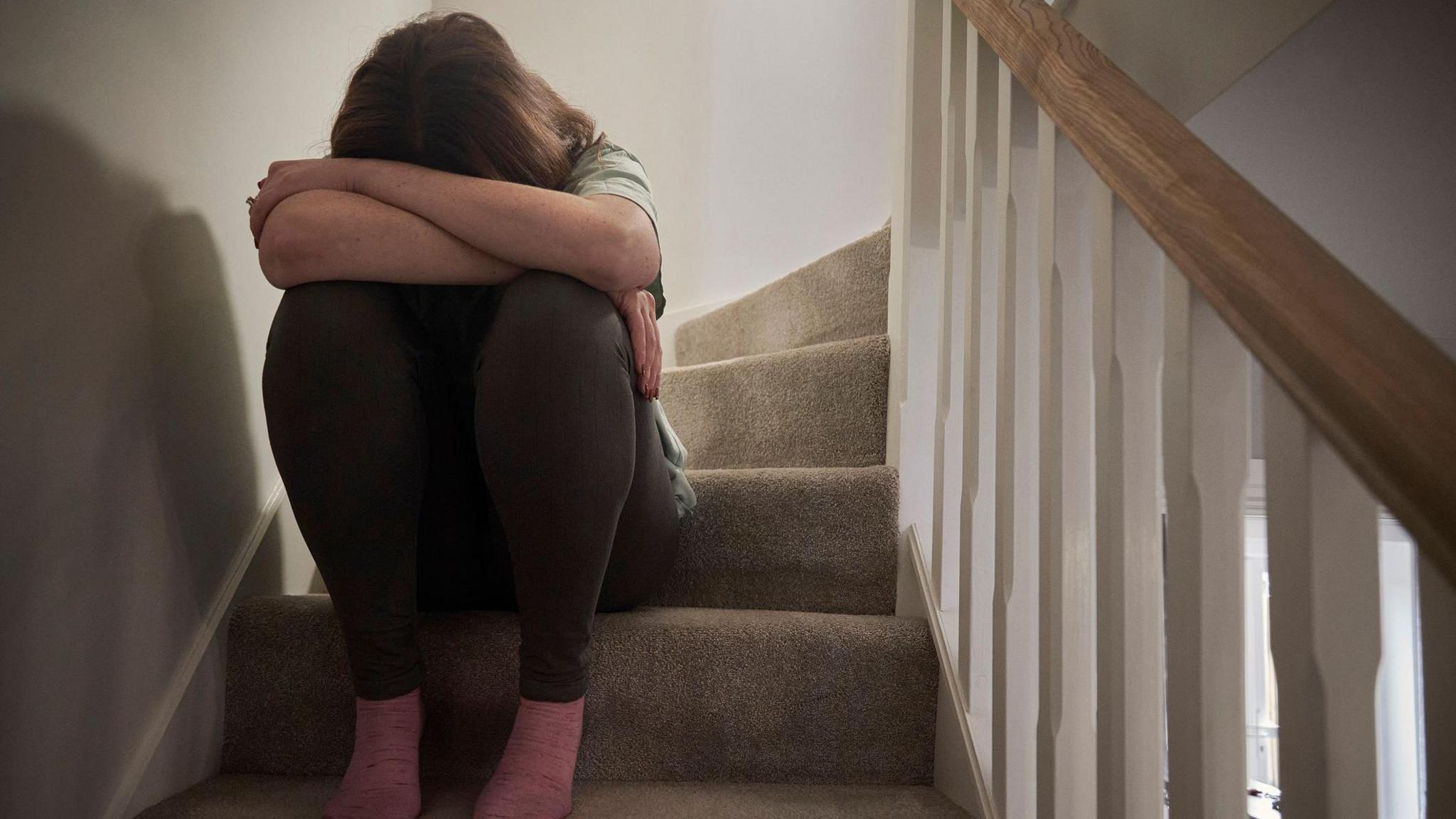 An upset woman sitting on some stairs with her head in her knees