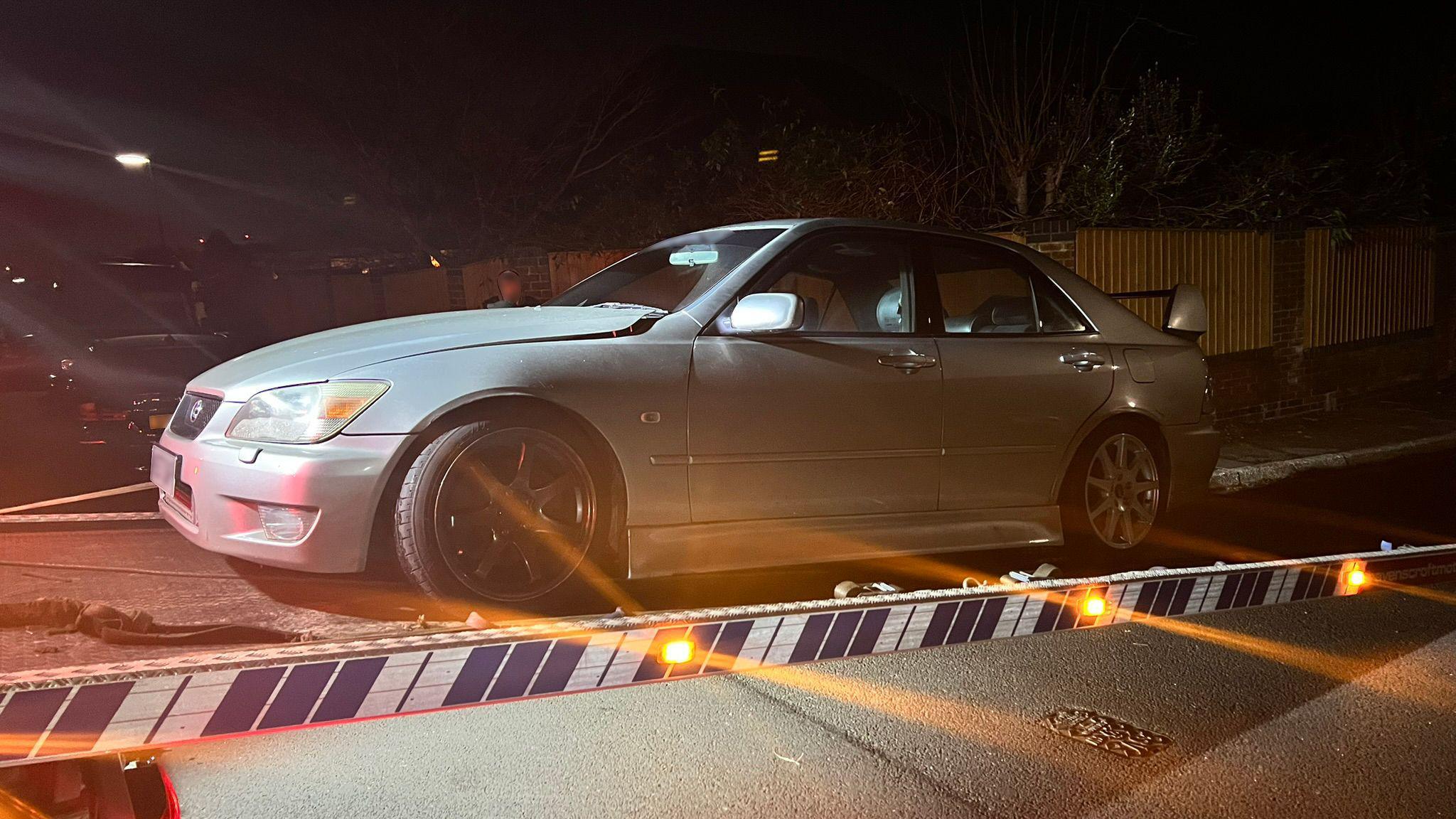 A silver Lexus IS 200 on the back of a flatbed truck at night time