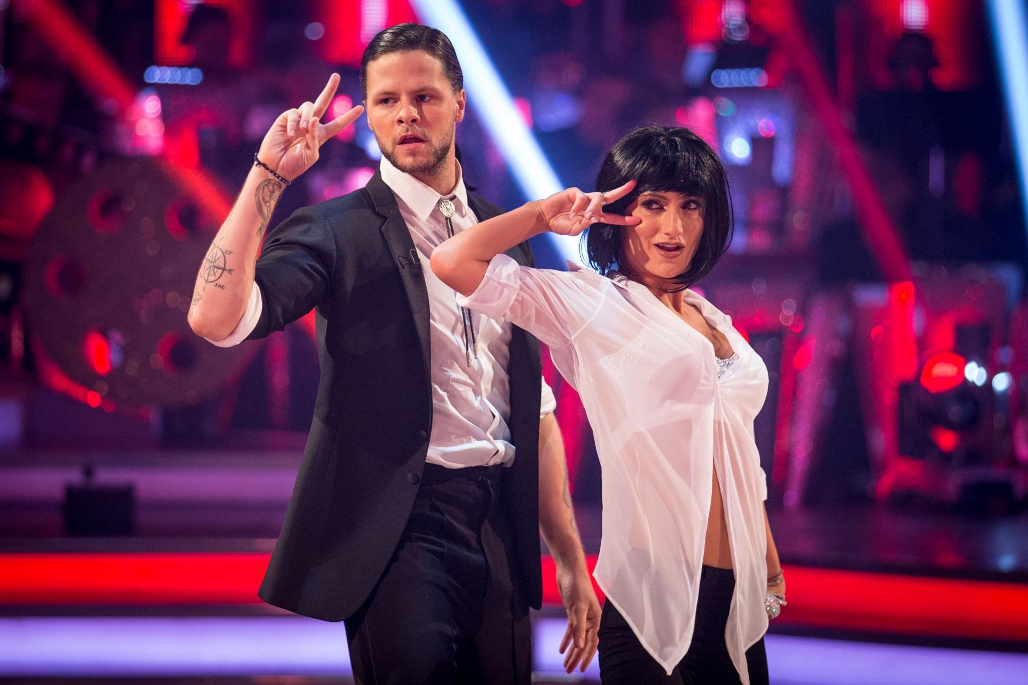 Jay McGuiness and Ailona Vilani posing with their fingers moving from the side of their heads, dressed as John Travolta and Uma Thurman's characters from the film Pulp Fiction performing the twist dance routine performed in the Jack Rabbit Slim's scene.