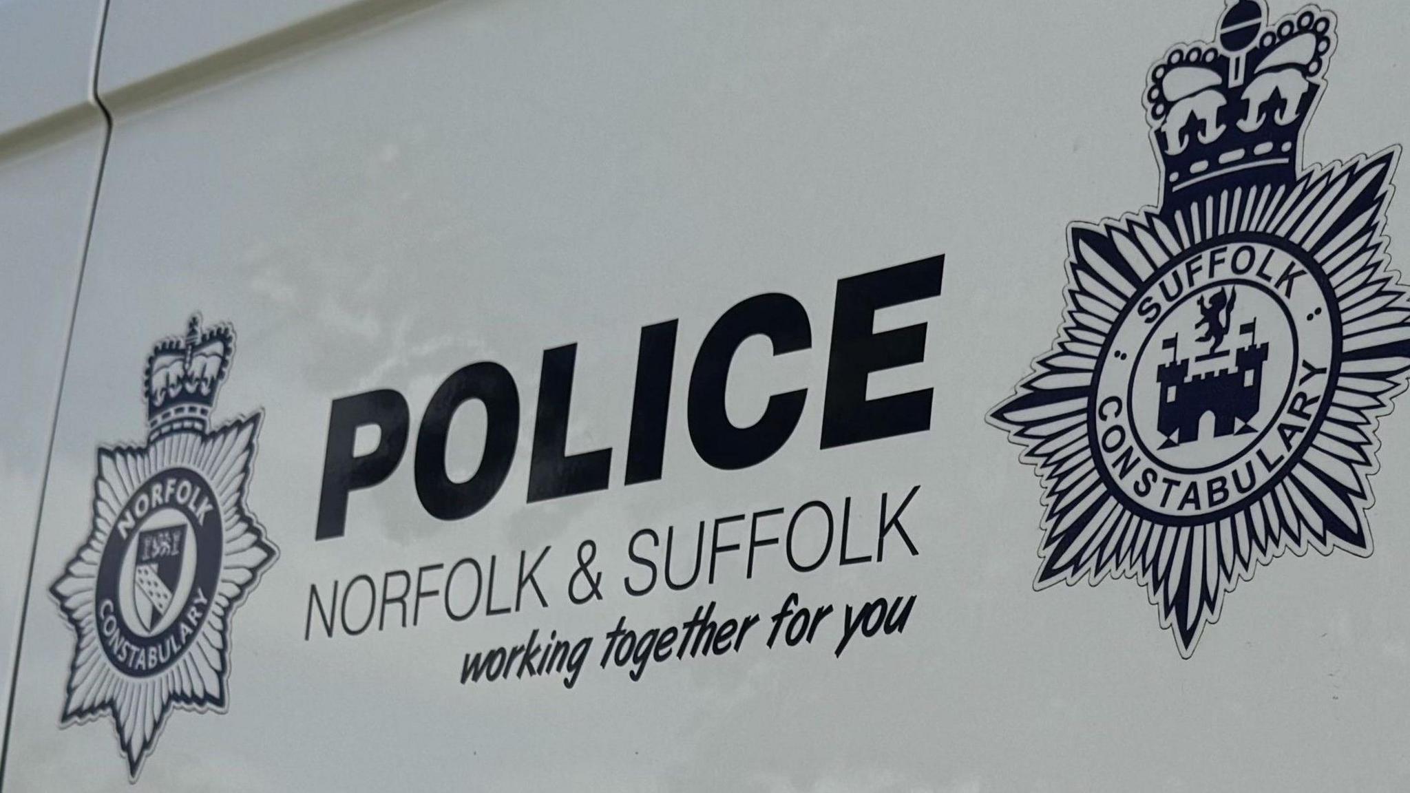 A close up of a white police van's logo that reads: Police, Norfolk & Suffolk, working together for you. Both police force's logos sit on each side of the writing.