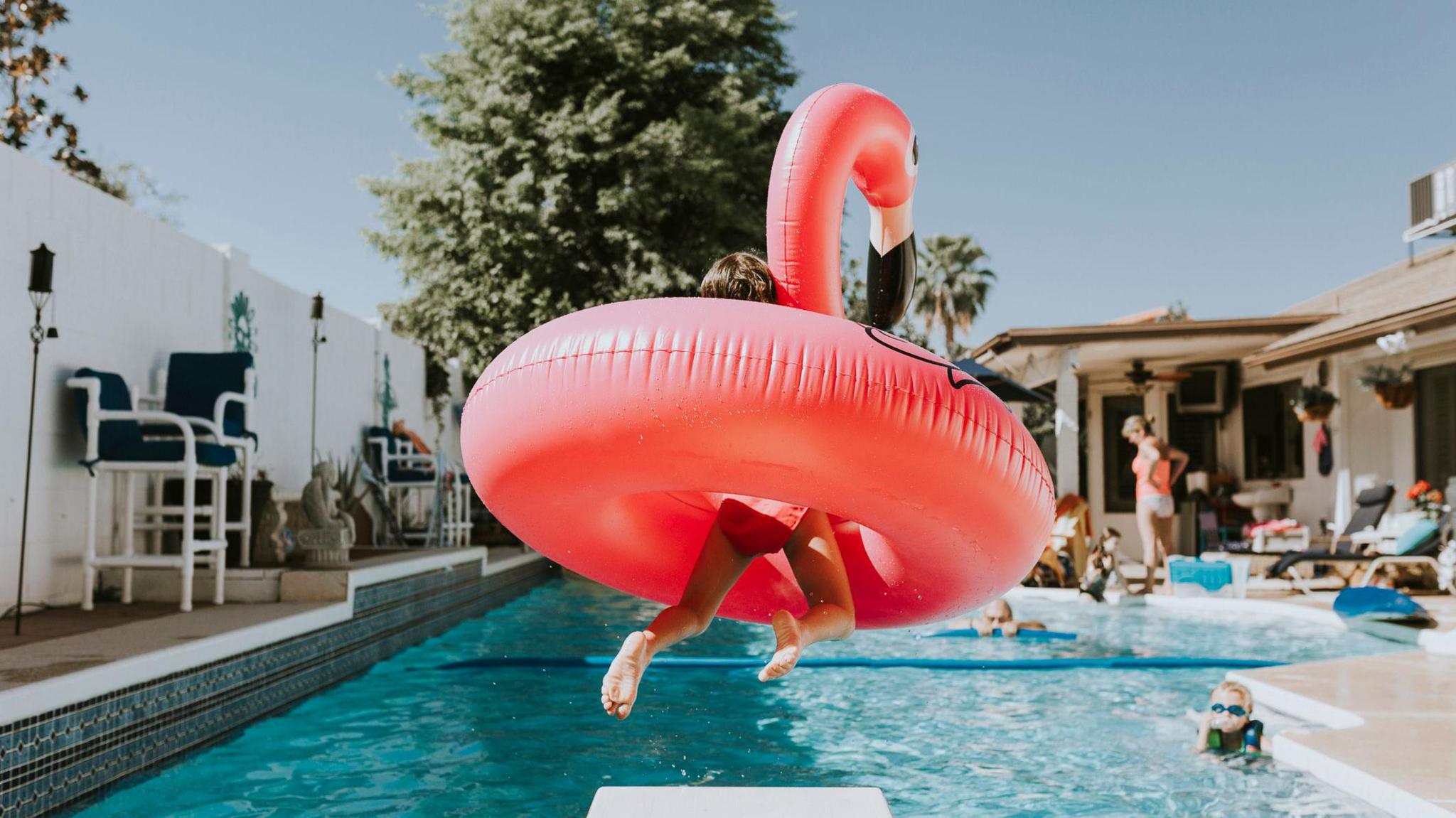 girl jumping into pool with flamingo inflatable