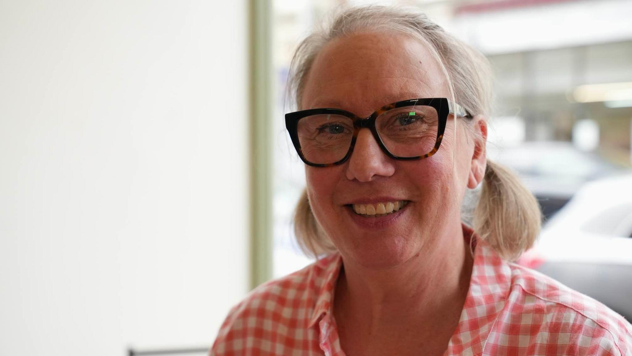 Lorraine Rodwell wearing a chequered shirt and glasses while smiling into the camera