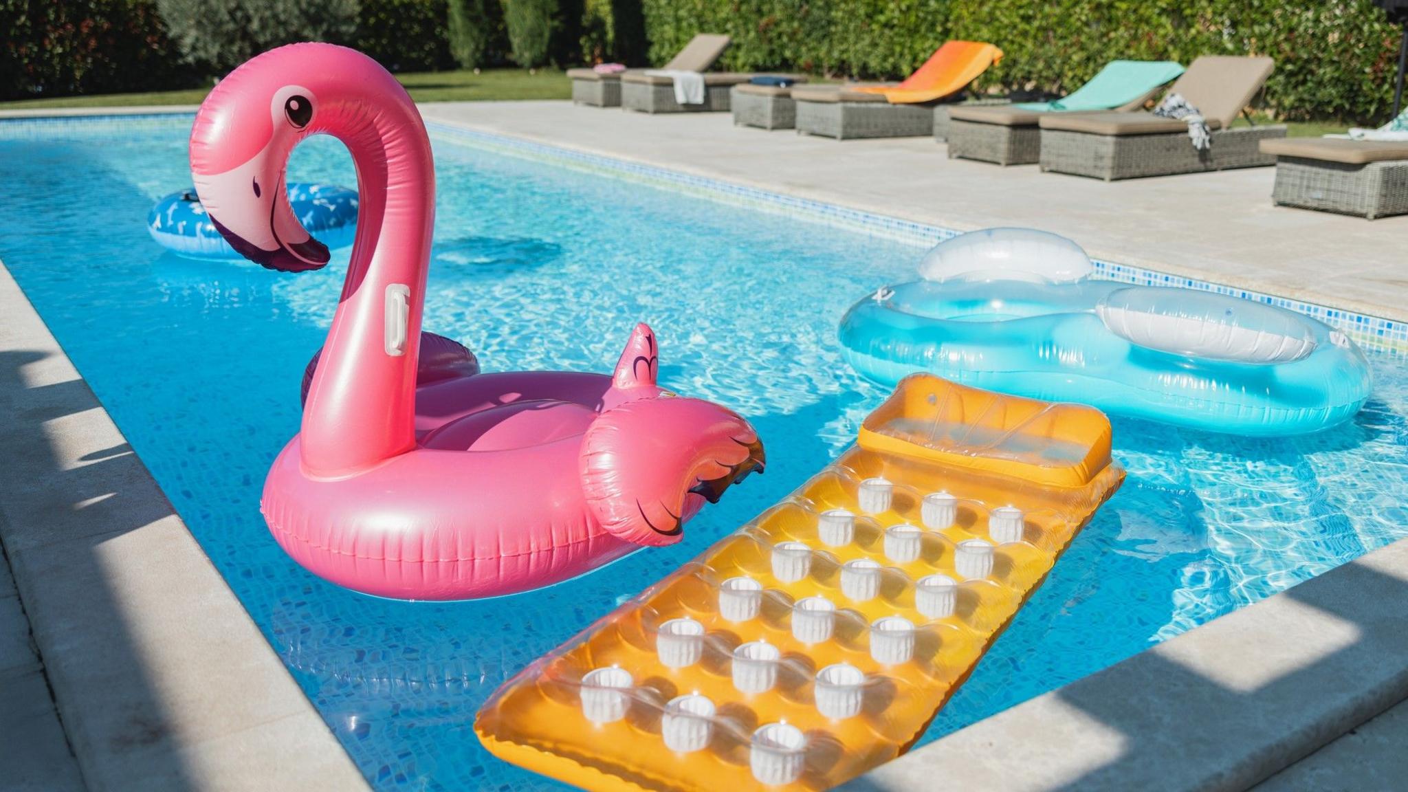 Two airbeds, an inflatable ring and an inflatable pink flamingo float in an empty pool.
