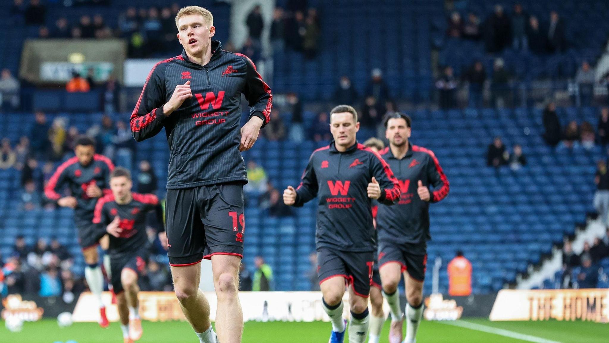 A photo of Millwall players running to warm up in their black and red away kits