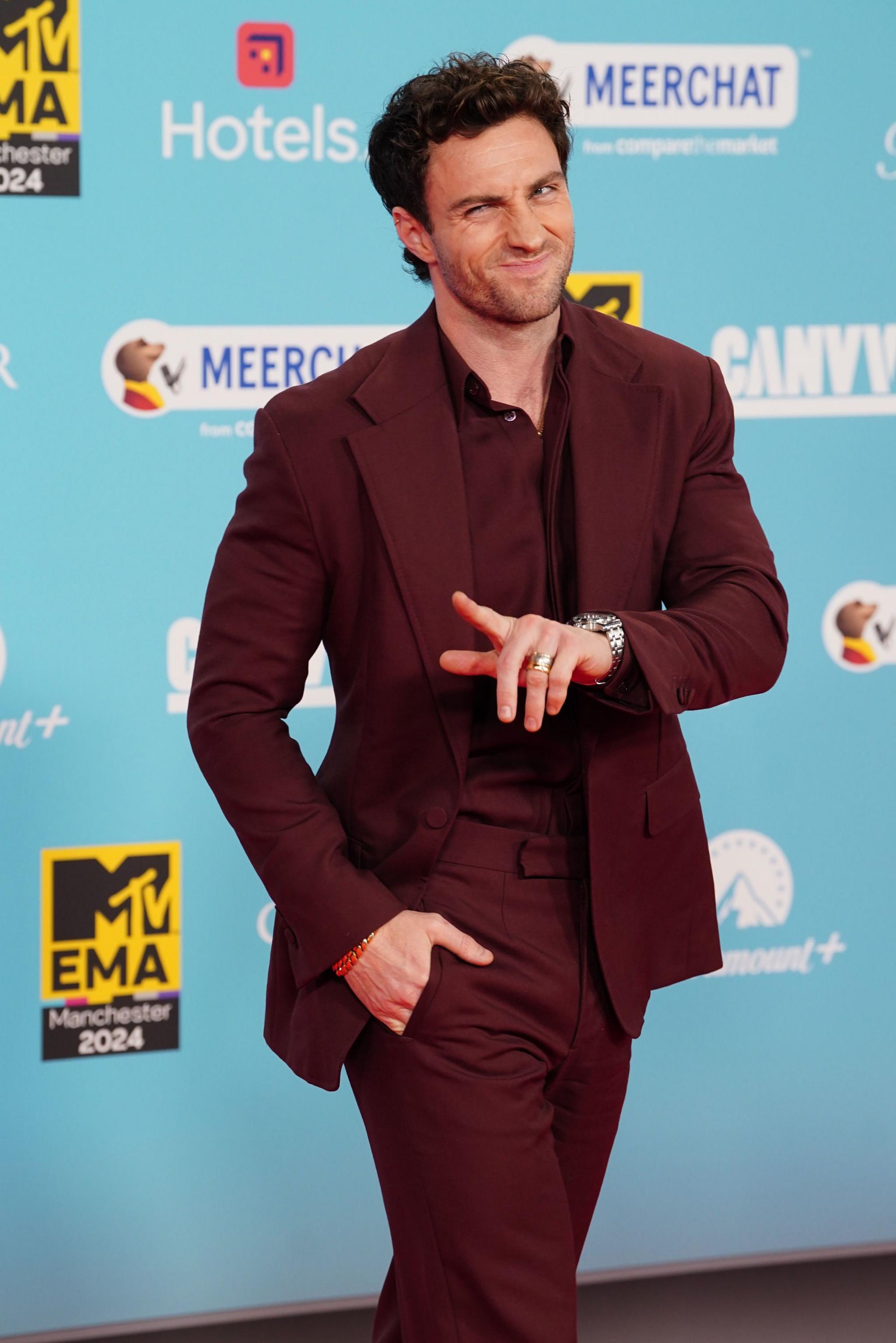 Aaron Taylor-Johnson winking and pointing in a burgundy suit