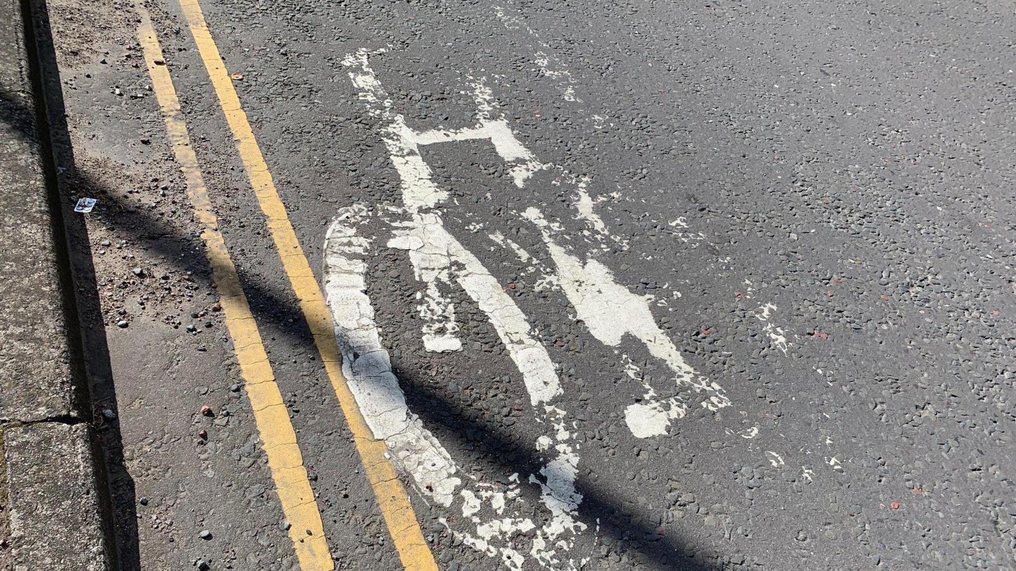 A faded bike path sign painted on the road in Dumfries