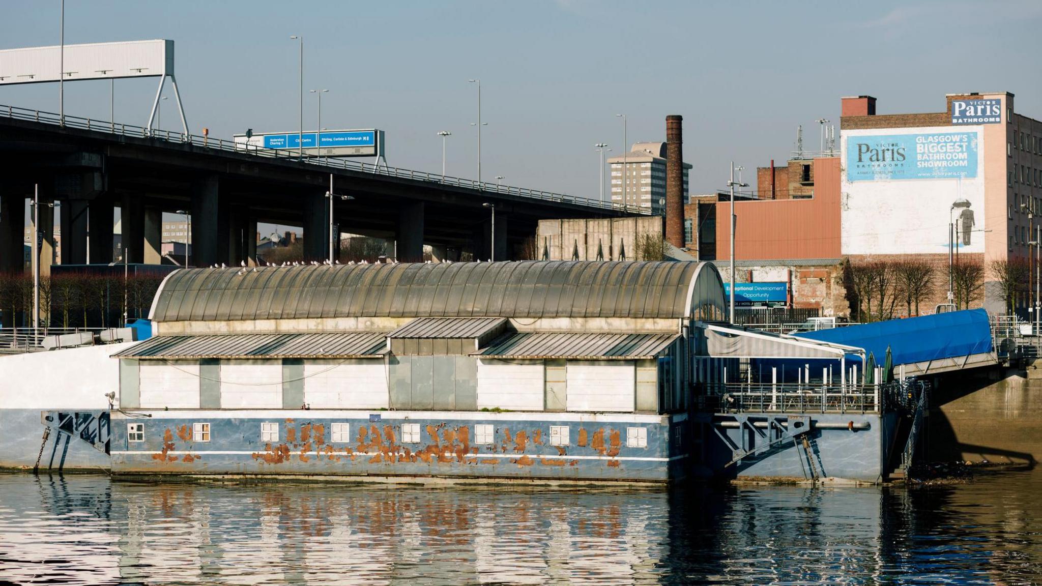 A blue and white floating structure, moored at the river bank