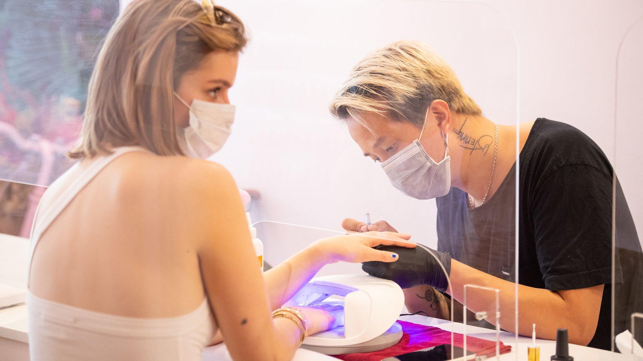 A nail technician at work behind a plastic protective screen at Coco Nails Club in London