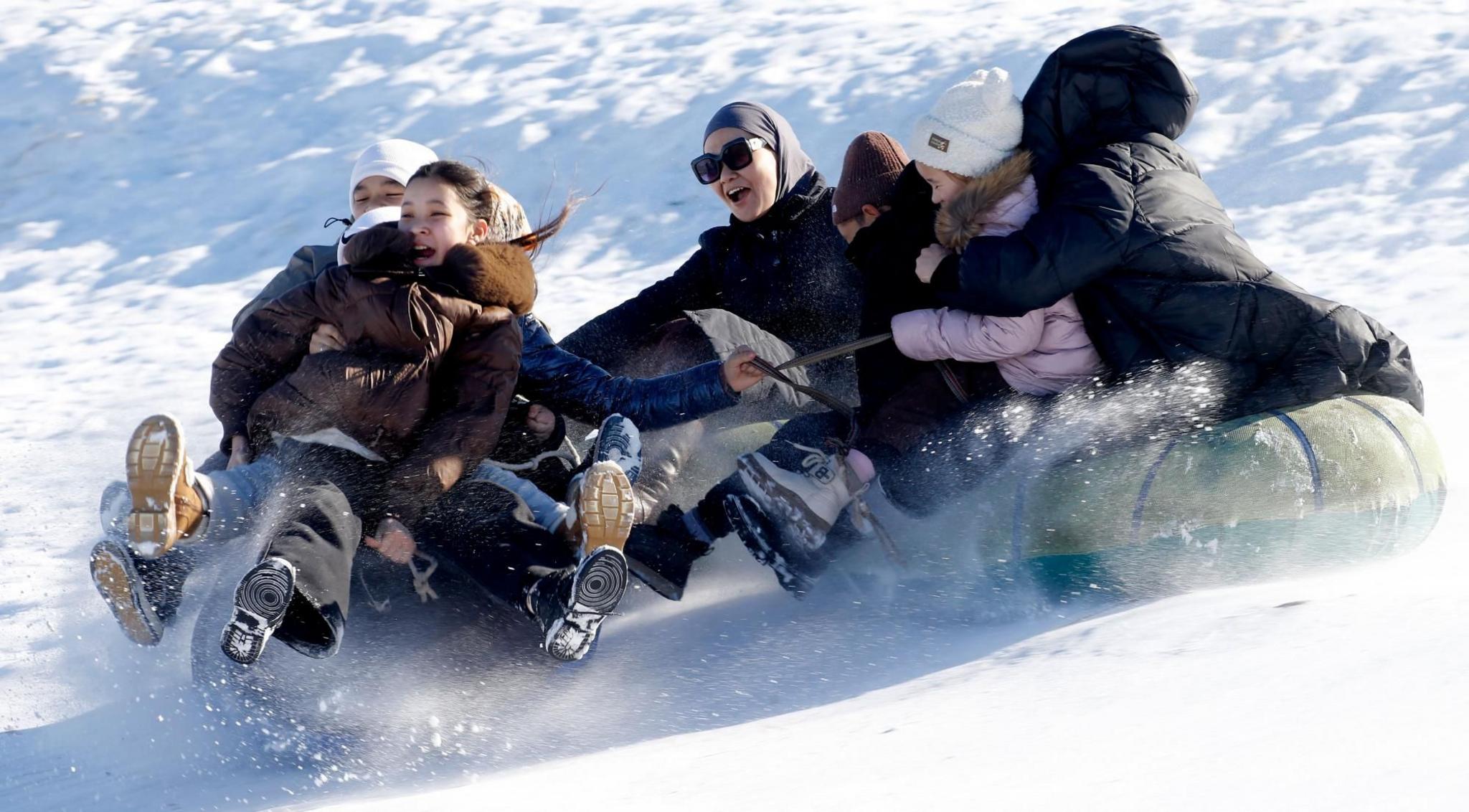 A group of people laughing while going down a snowy slope on a sledge