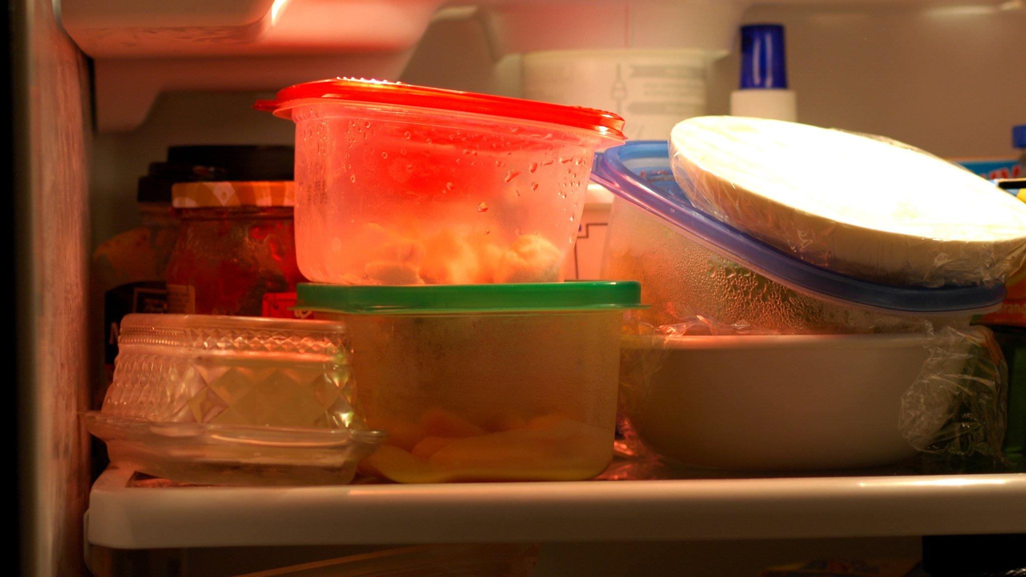 Interior of a fridge stuffed with tubs and plates of leftovers