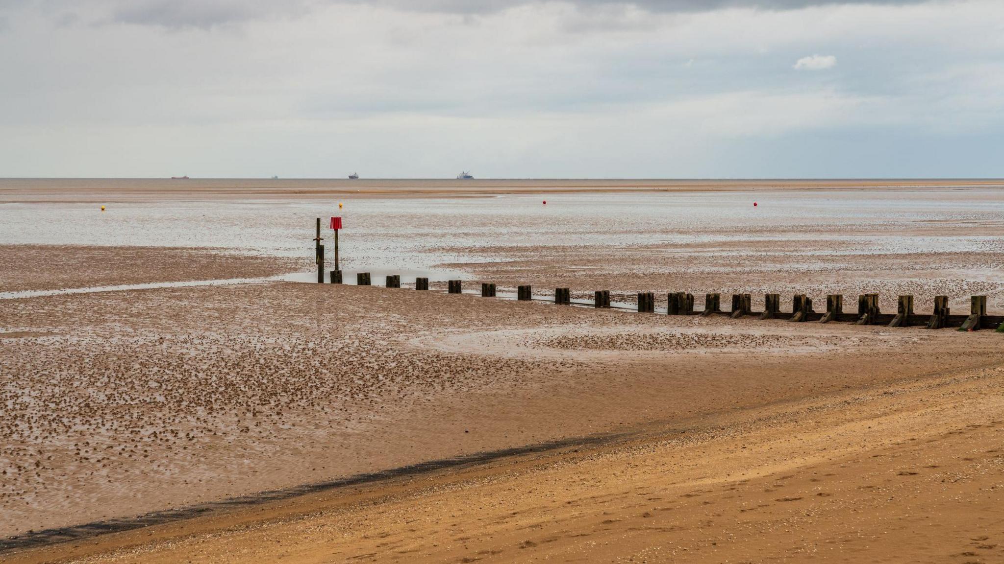 A photo of a Cleethorpes beach. The tide is out and the sky is blue with light clouds. 