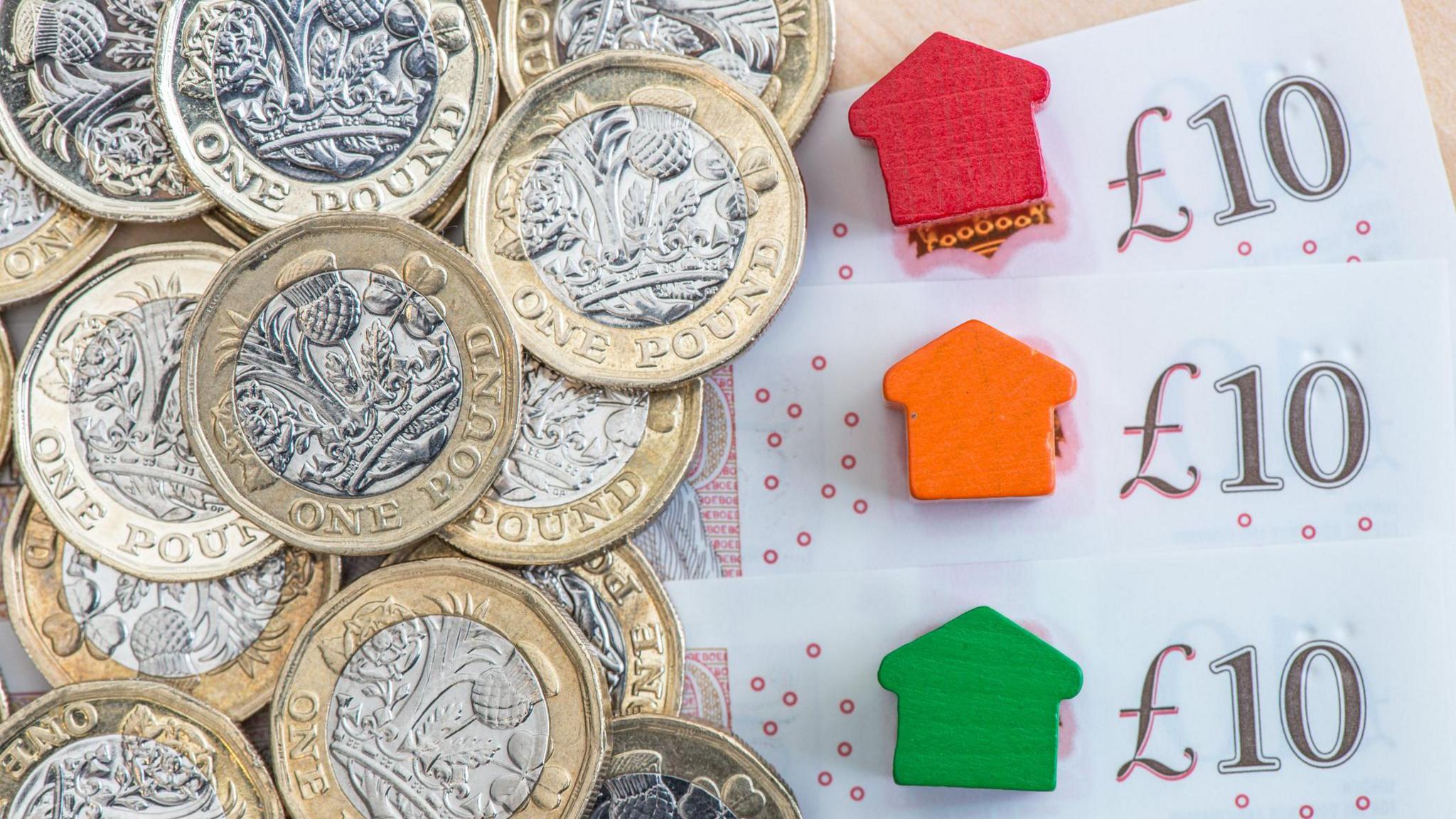 Pile of notes and coins and small wooden representations of houses.