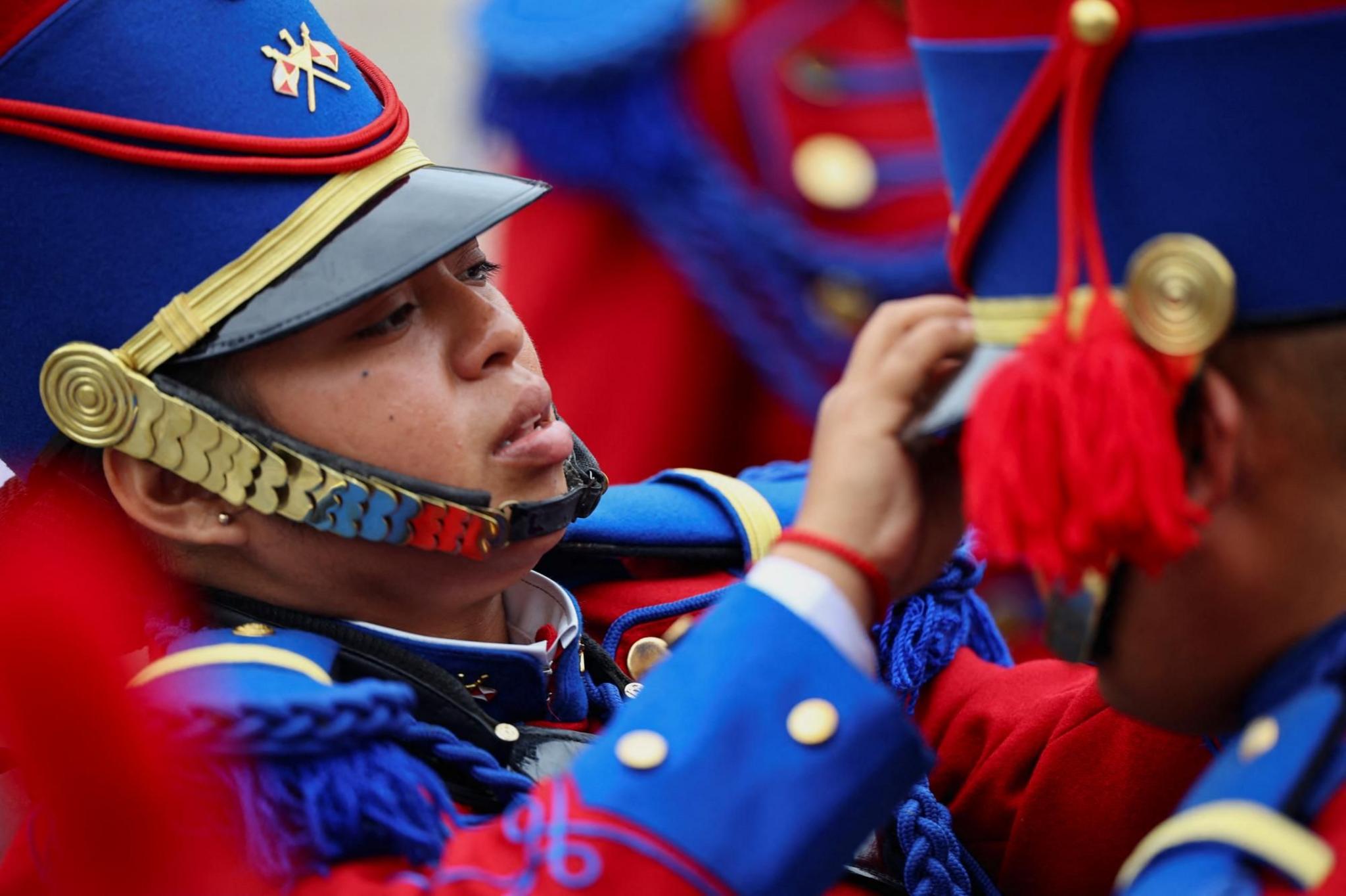 A member of the Husares de Junin regiment adjusts another soldier's hat 