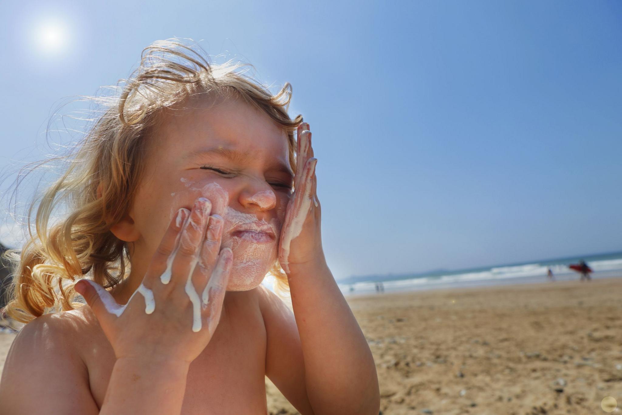 Child rubbing sun cream into their face on a beach