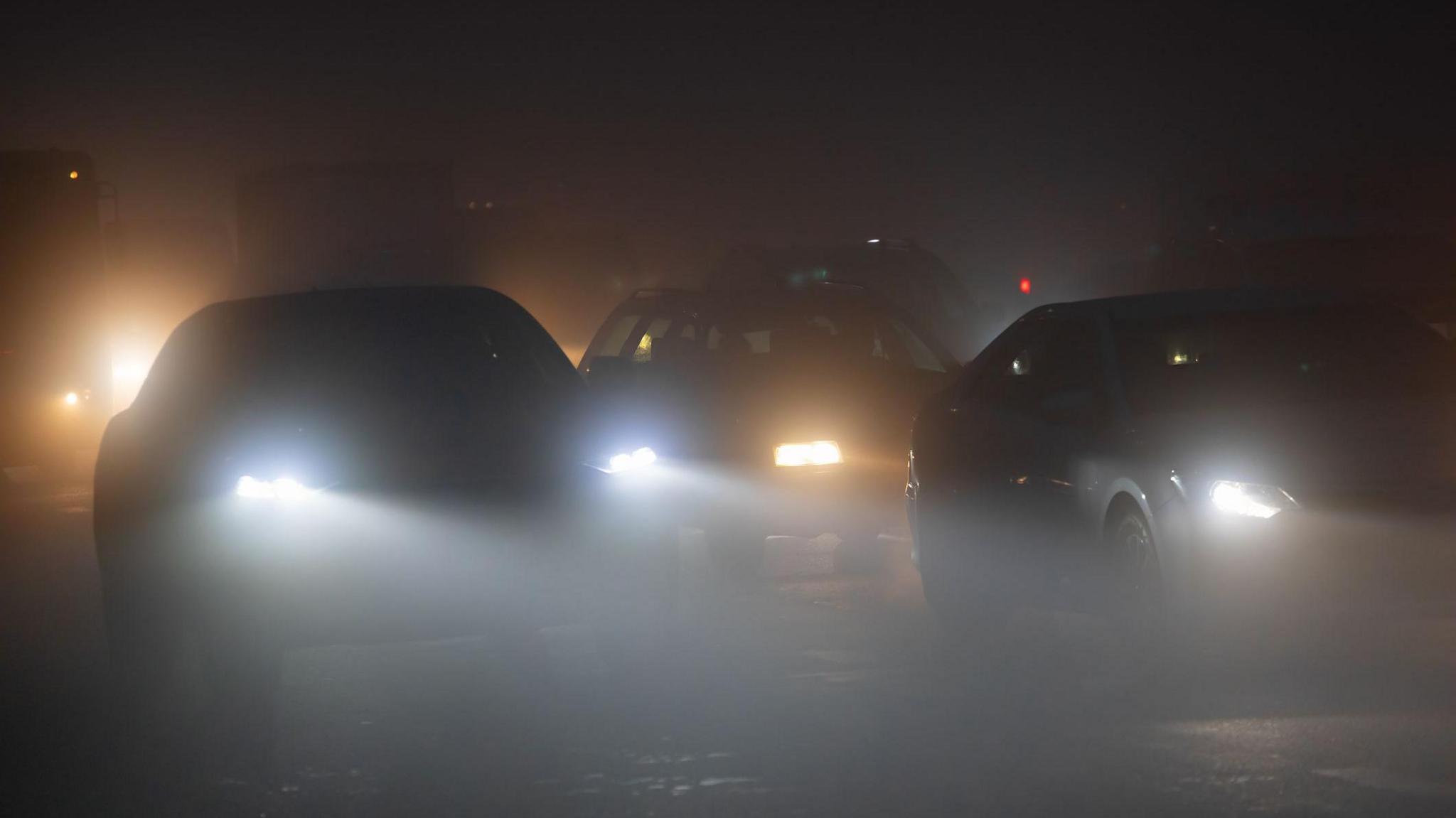 Three sets of car headlights shining in the dark