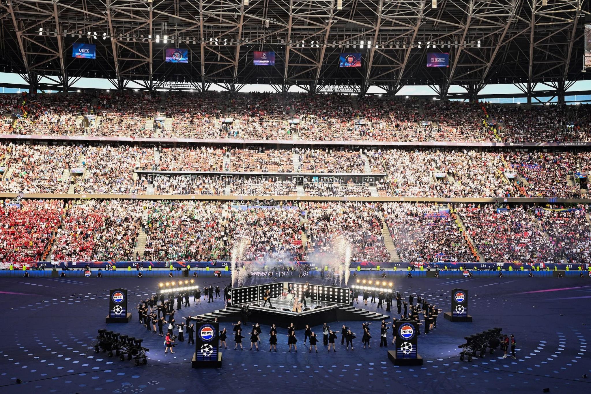 Picture of the stage at the Puskas Arena, Budapest. A large stand of crowds is seen in the backgorund of a stage in the middle of the pitch.