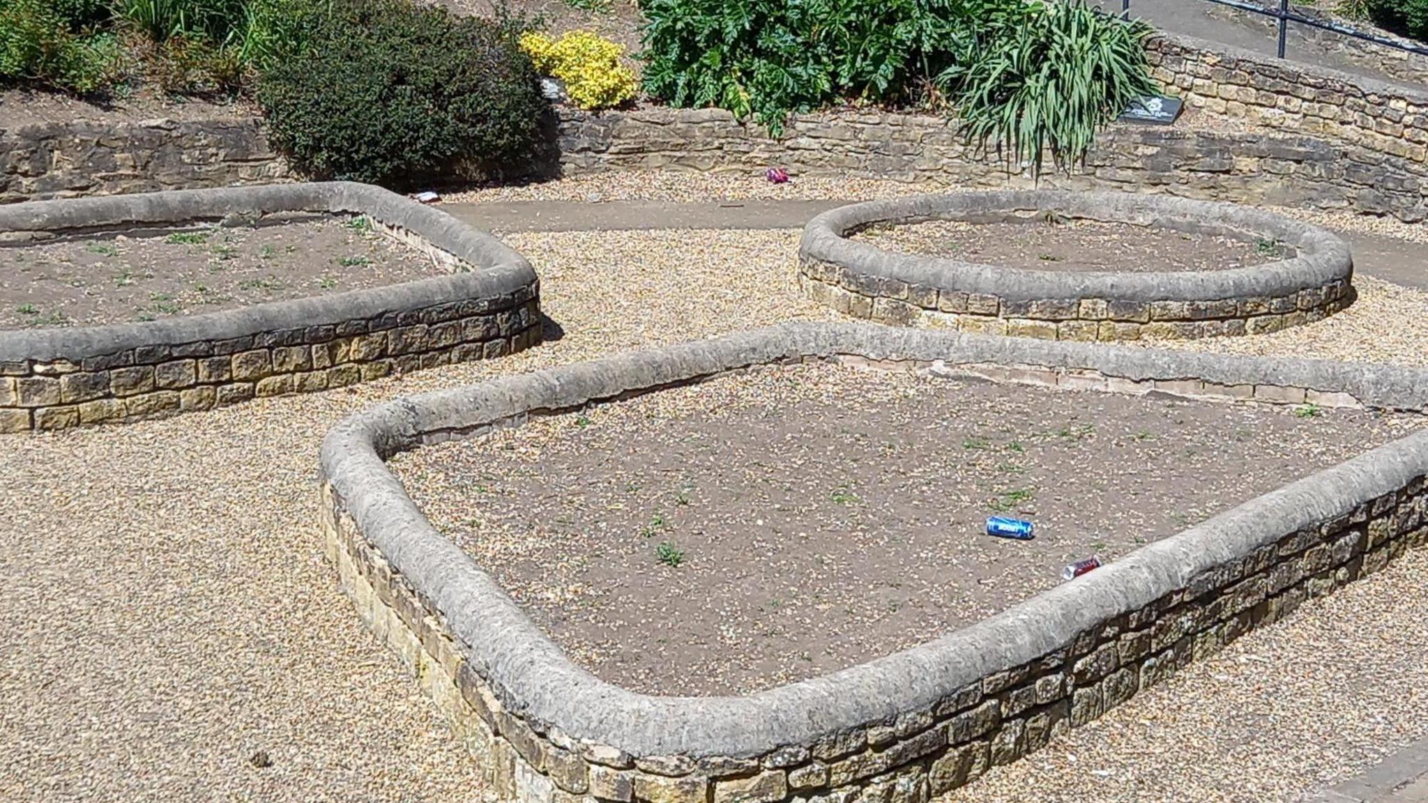 A walled section of the garden - with a round raised bed with soil and freshly planted bushes.