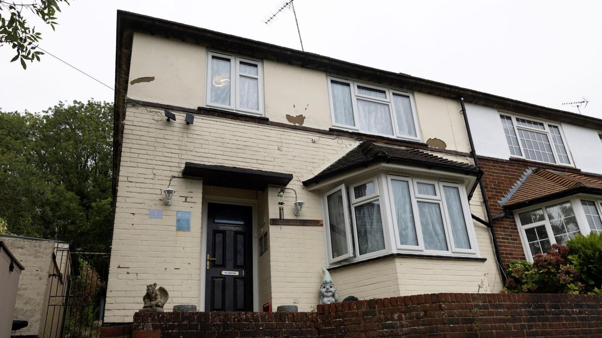 The exterior of a two-storey brick house painted in cream-coloured paint, viewed from the front.