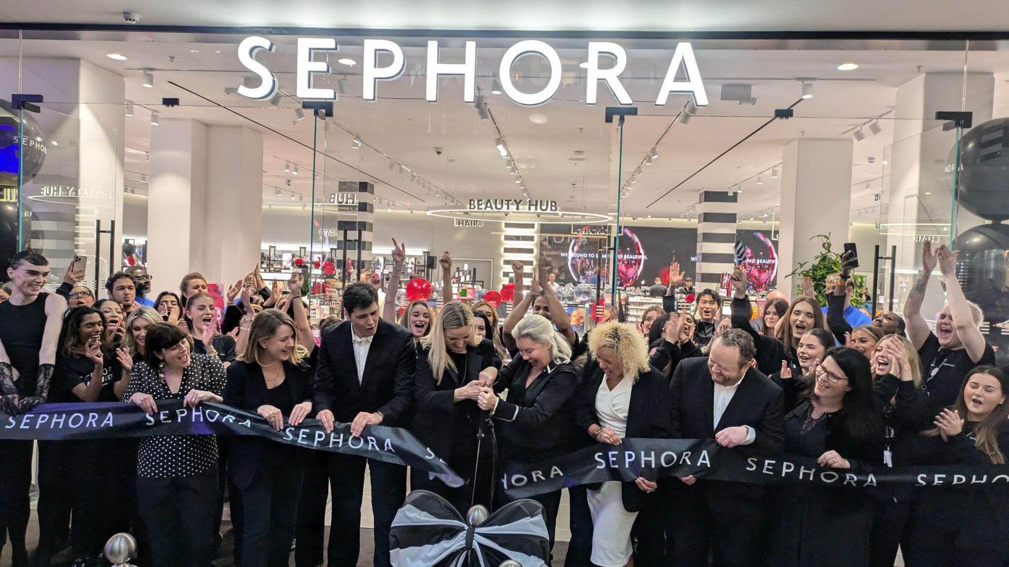 A group of people in black shirts cutting the black ribbon in front of the glass-fronted shop, which says "Sephora" in white letters.