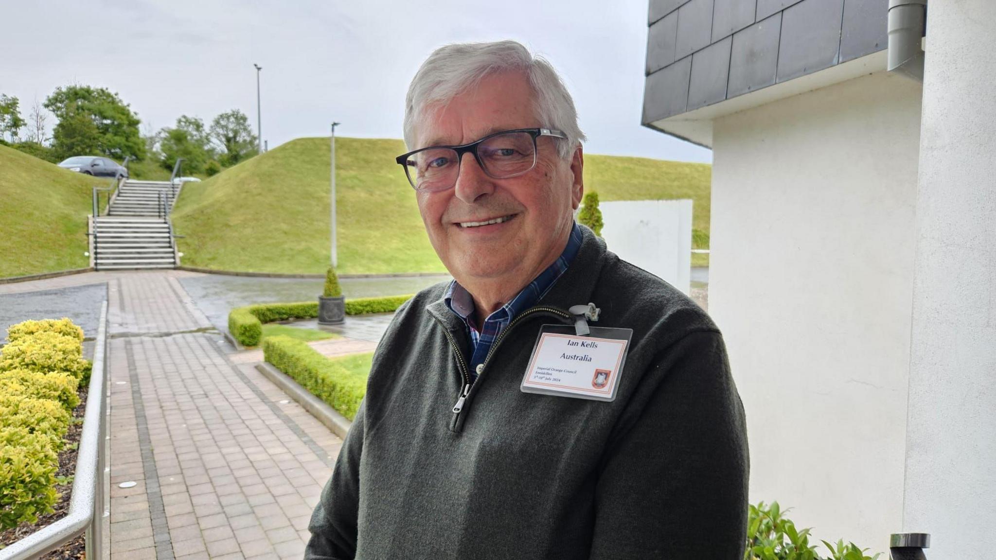 Ian Kells, centre of the photo, taken outdoors, with a path and grass in the background