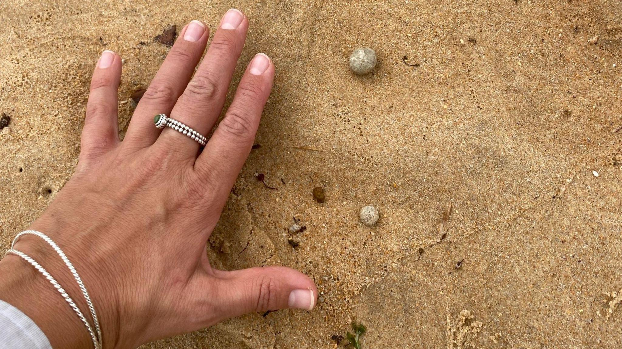 Two small grey balls in sand with a hand for size reference