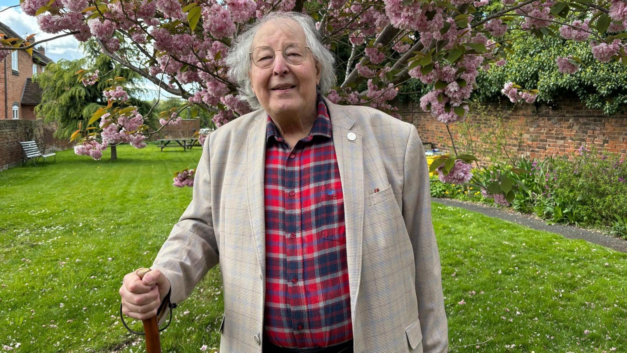 Mike Kean-Price standing beneath a floral tree with a walking stick