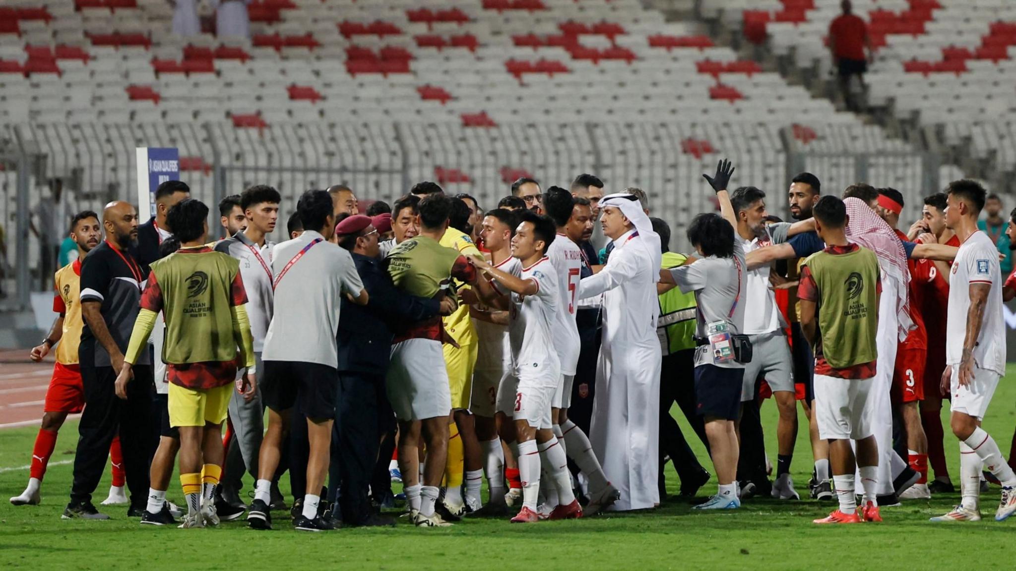 Around twenty players, coaches and officials on a football pitch, engaged in a mass brawl.