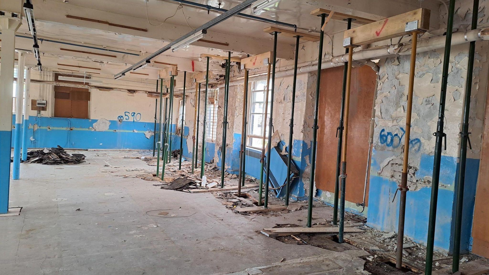 An internal view of an old mill with scaffolding holding up the ceiling and graffiti on the walls